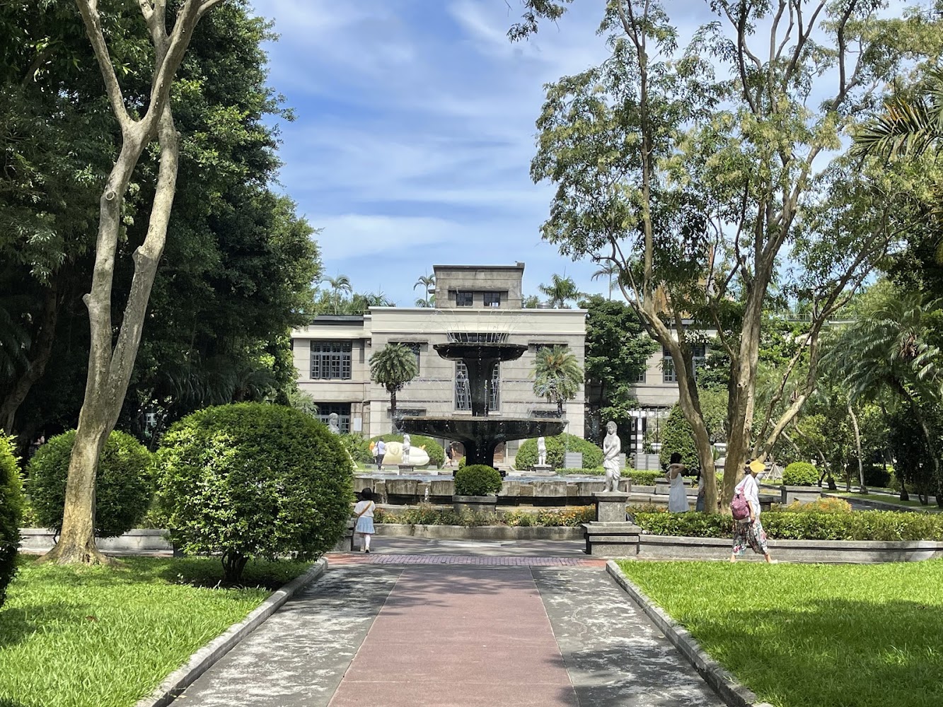 融合西洋風格的大樓前方是一個有雕像和噴水池的花園，四周綠樹成蔭，有行人悠閒地在步道上散步，環境十分優美寧靜。
