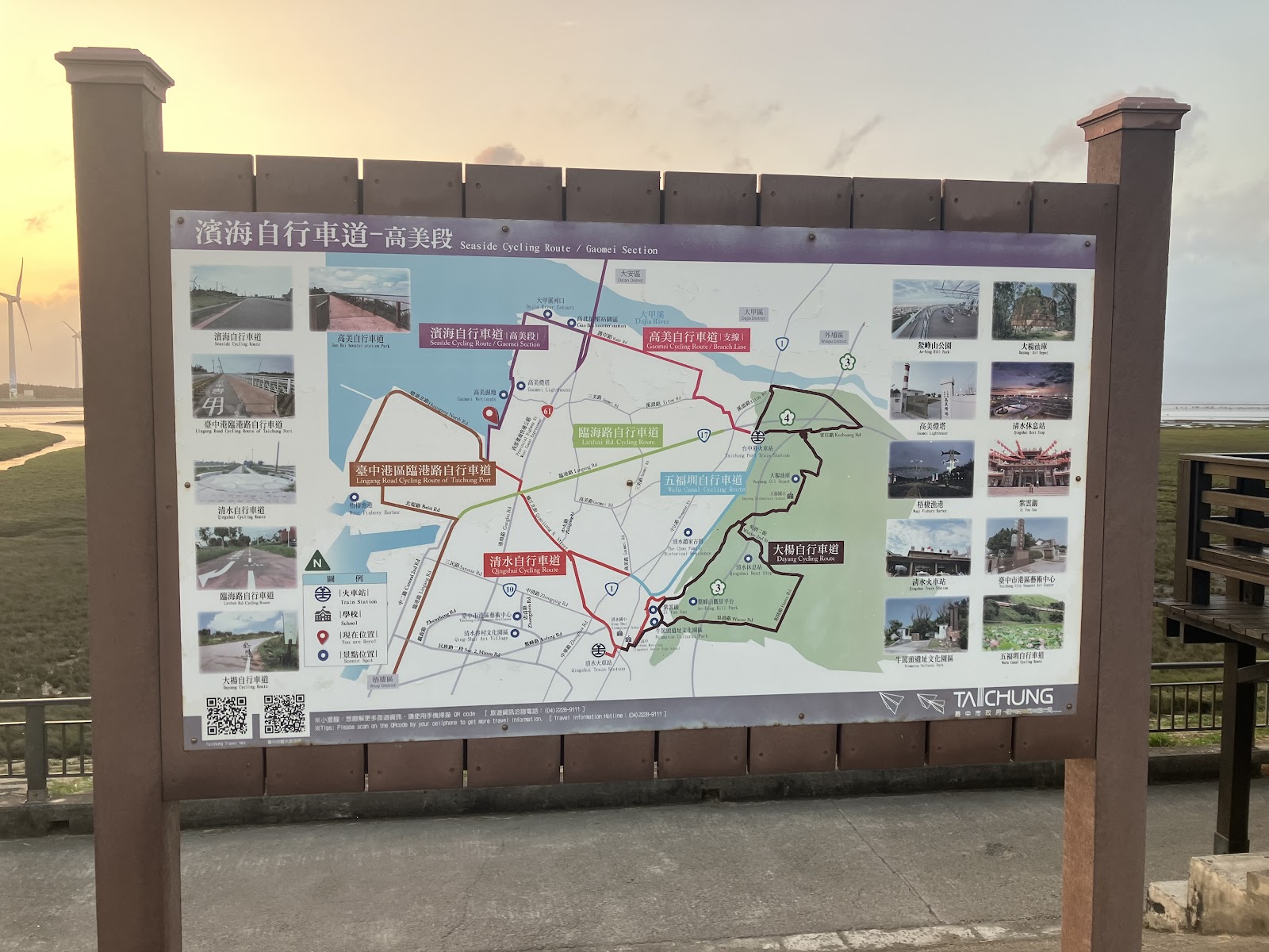台中濱海自行車道高美段路線指示牌,背景夕陽橙紅,遠方風機