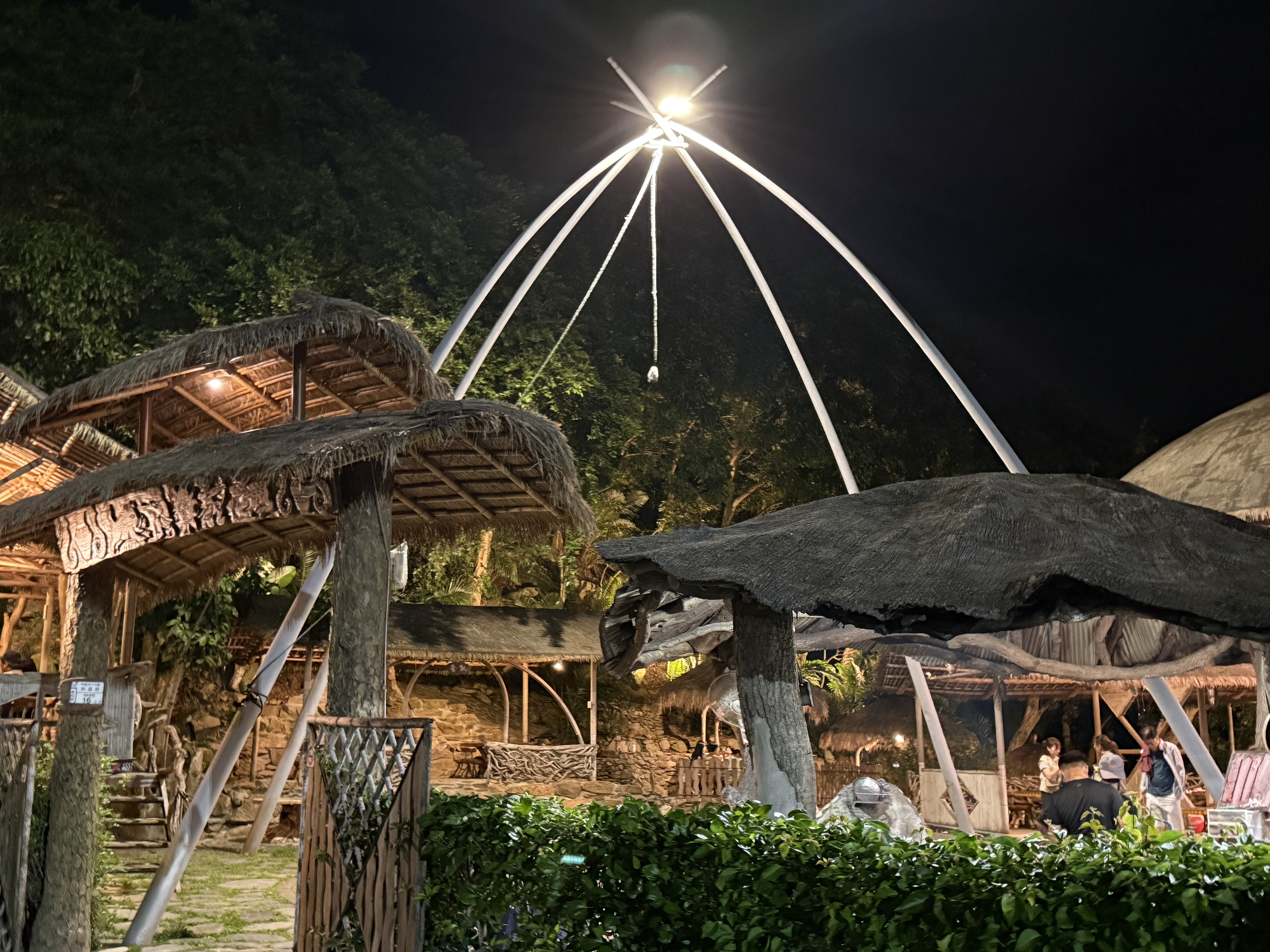 夜晚的戶外景點，有茅草屋頂、木製建築和拱形結構，燈光點亮