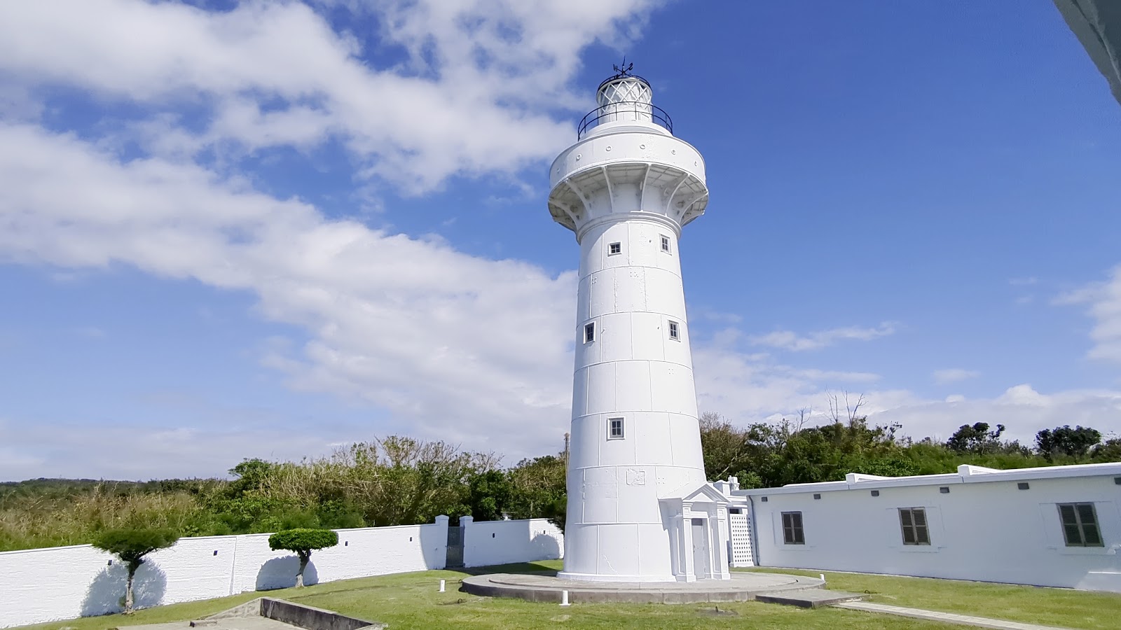 近距離仰拍鵝鑾鼻燈塔白色圓柱塔身全景，藍天白雲相映成輝