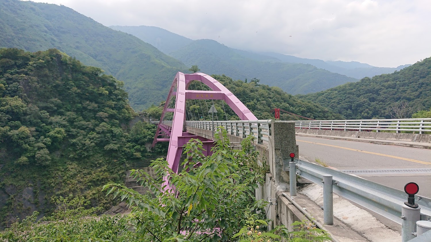 粉紫色拱橋橫跨青山綠樹之間