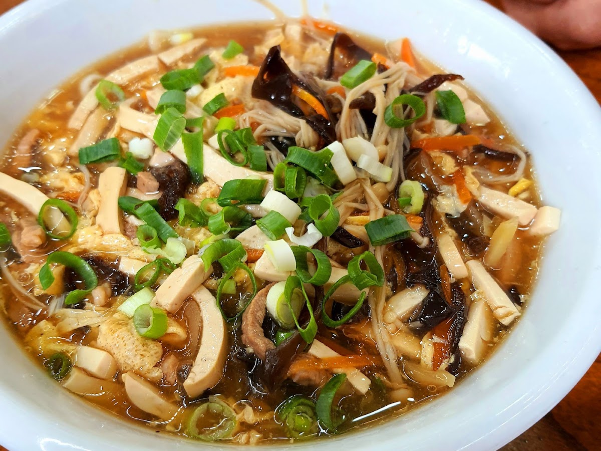 十一街酸辣湯，白碗盛著深棕色酸辣湯，配料有木耳、豆腐、蔬菜，撒蔥花