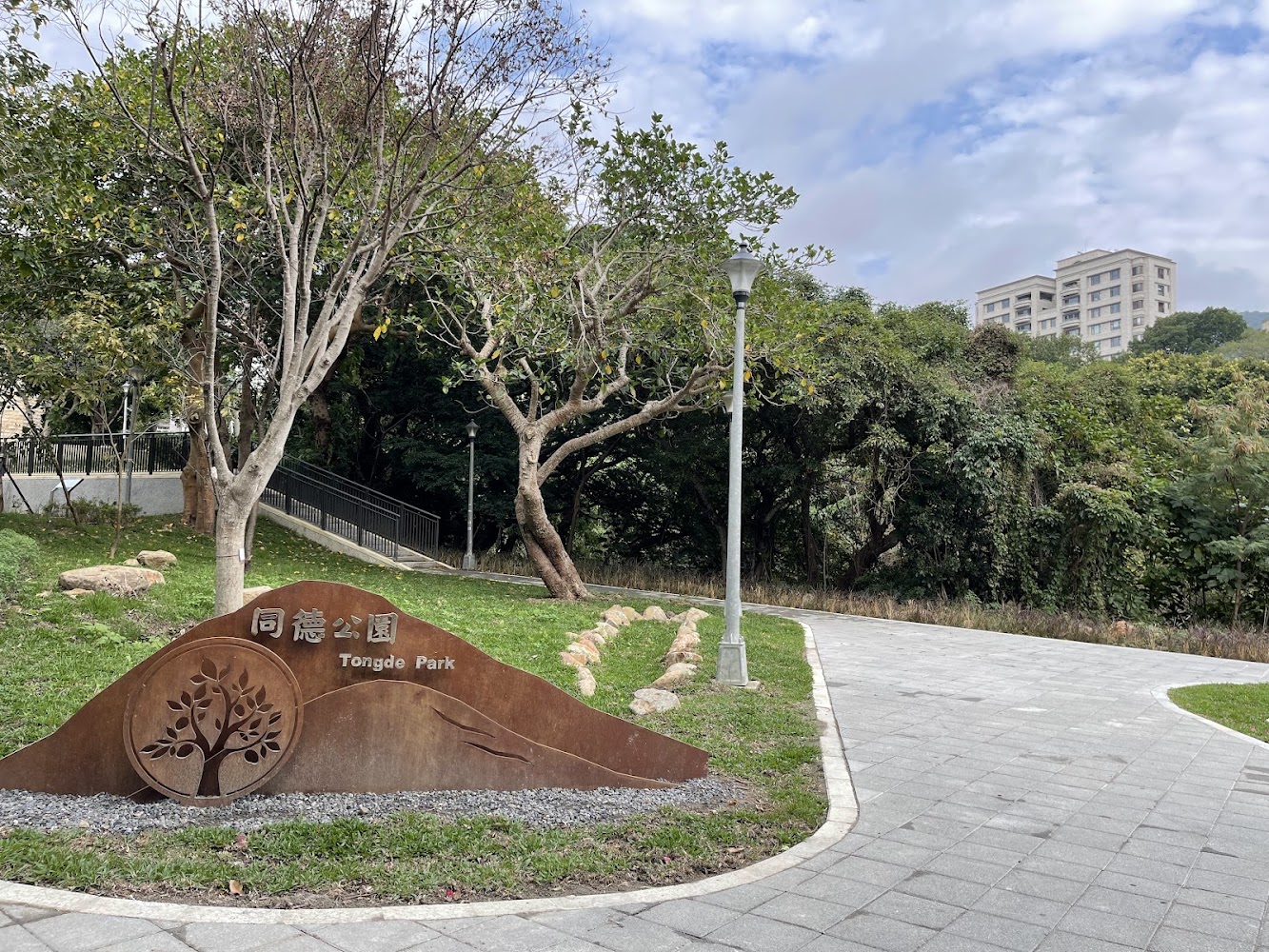 同德公園入口，有公園標誌、樹木、路燈與彎曲步道