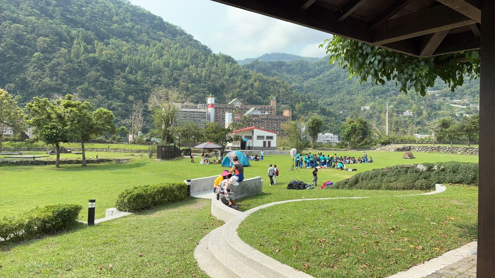 東遊季溫泉渡假村寬闊草坪，假日遊客在草地上紮營與戶外活動，後方可見旅館建築與翠綠山巒