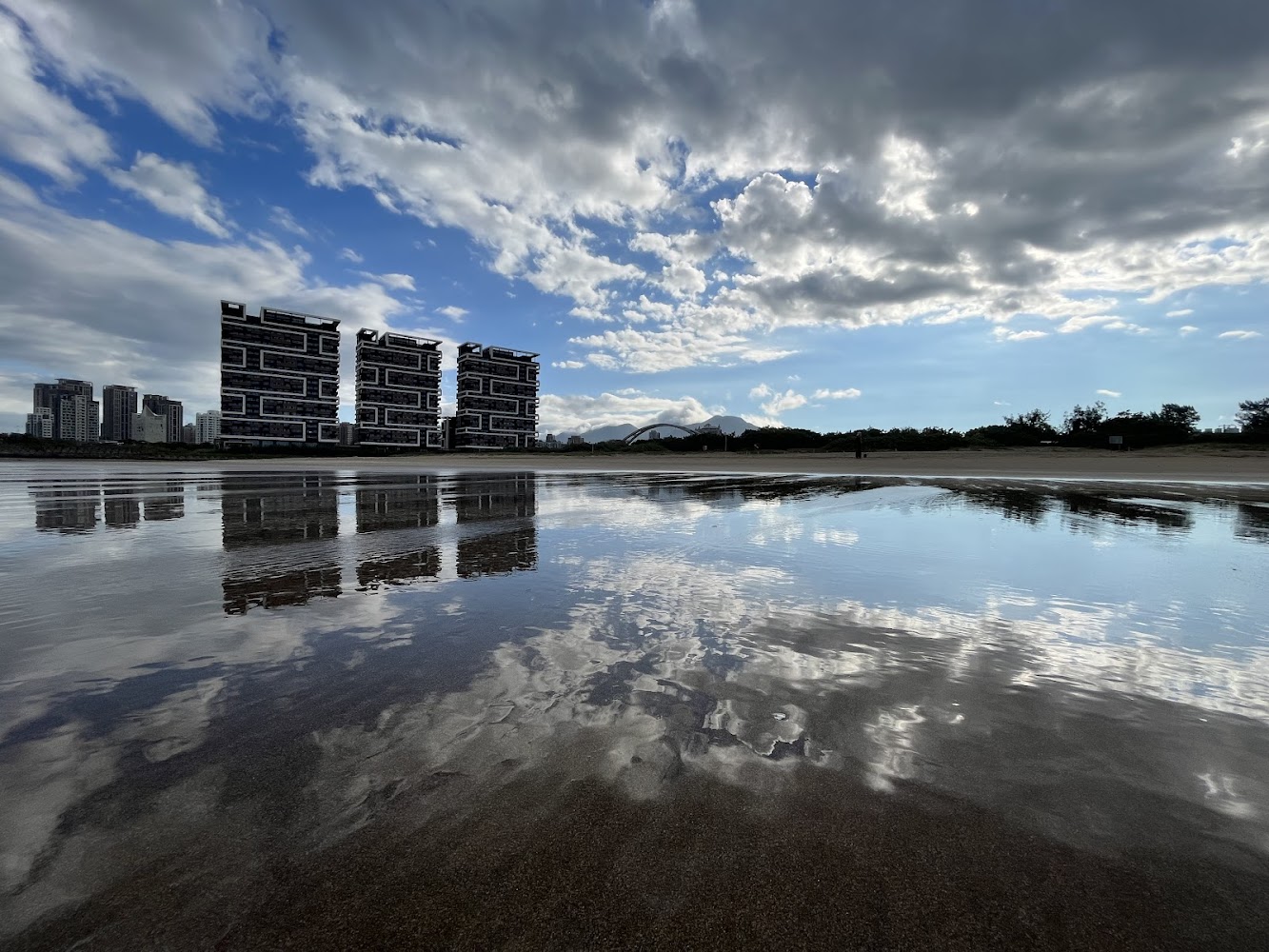 水面映出天空倒影，背景有特色高樓建築的沙崙海水浴場景色