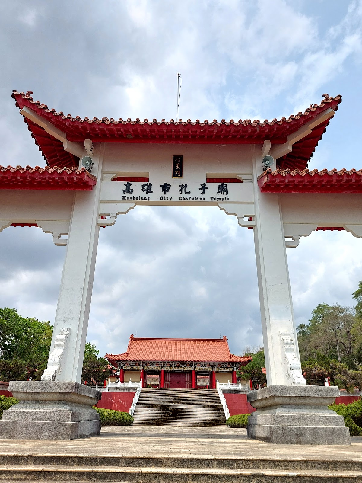 旗山孔子廟白色牌坊仰拍，透過牌坊可見紅色正殿，高大石階