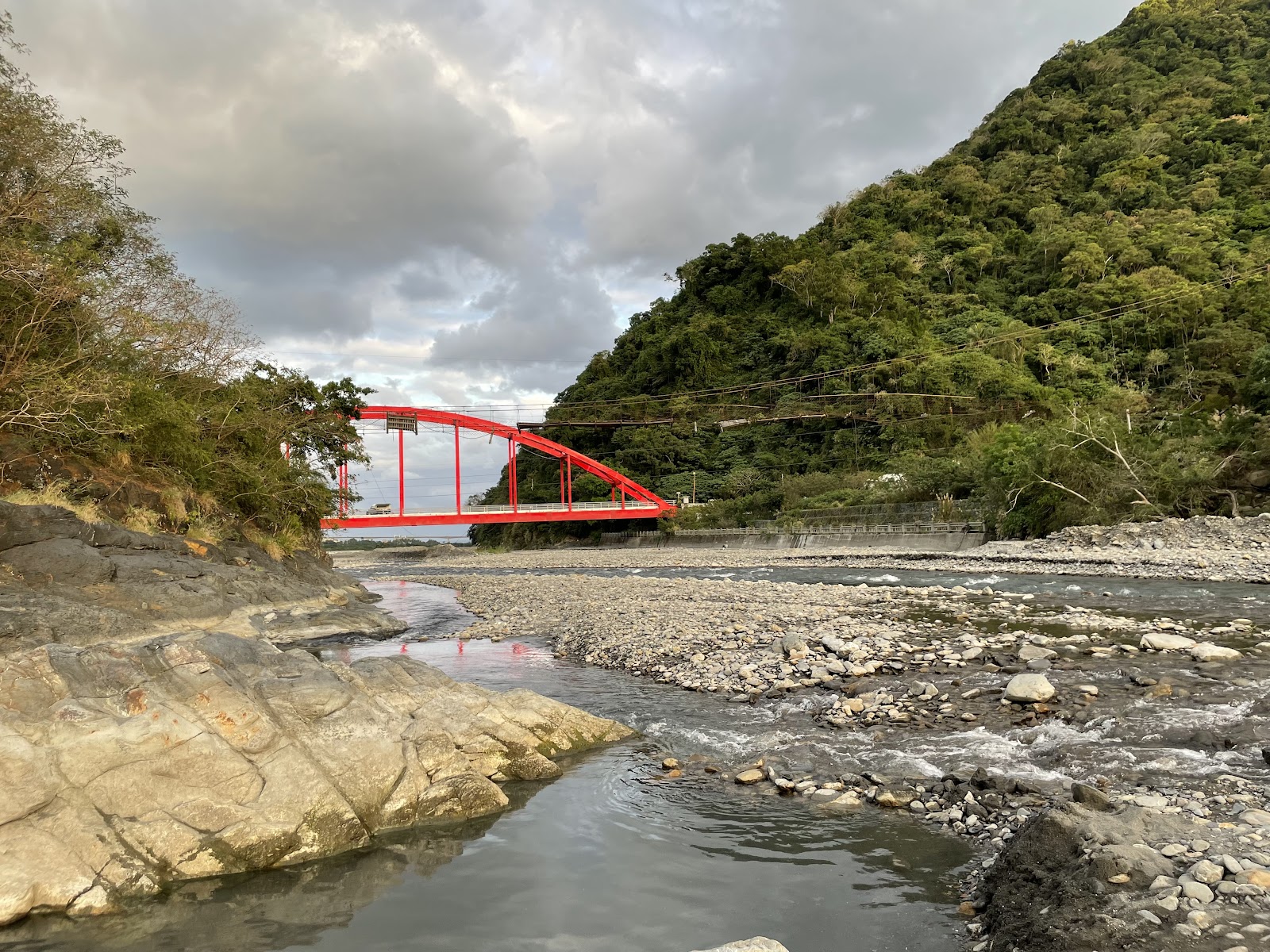 從溪床仰視金崙溫泉虹橋,清澈溪水流過岩石,背景青山環繞