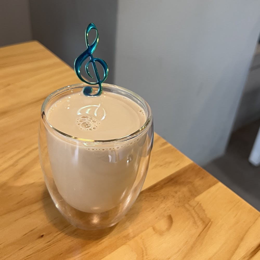 一杯奶茶，杯中插有藍色音符攪拌棒，放在木桌上