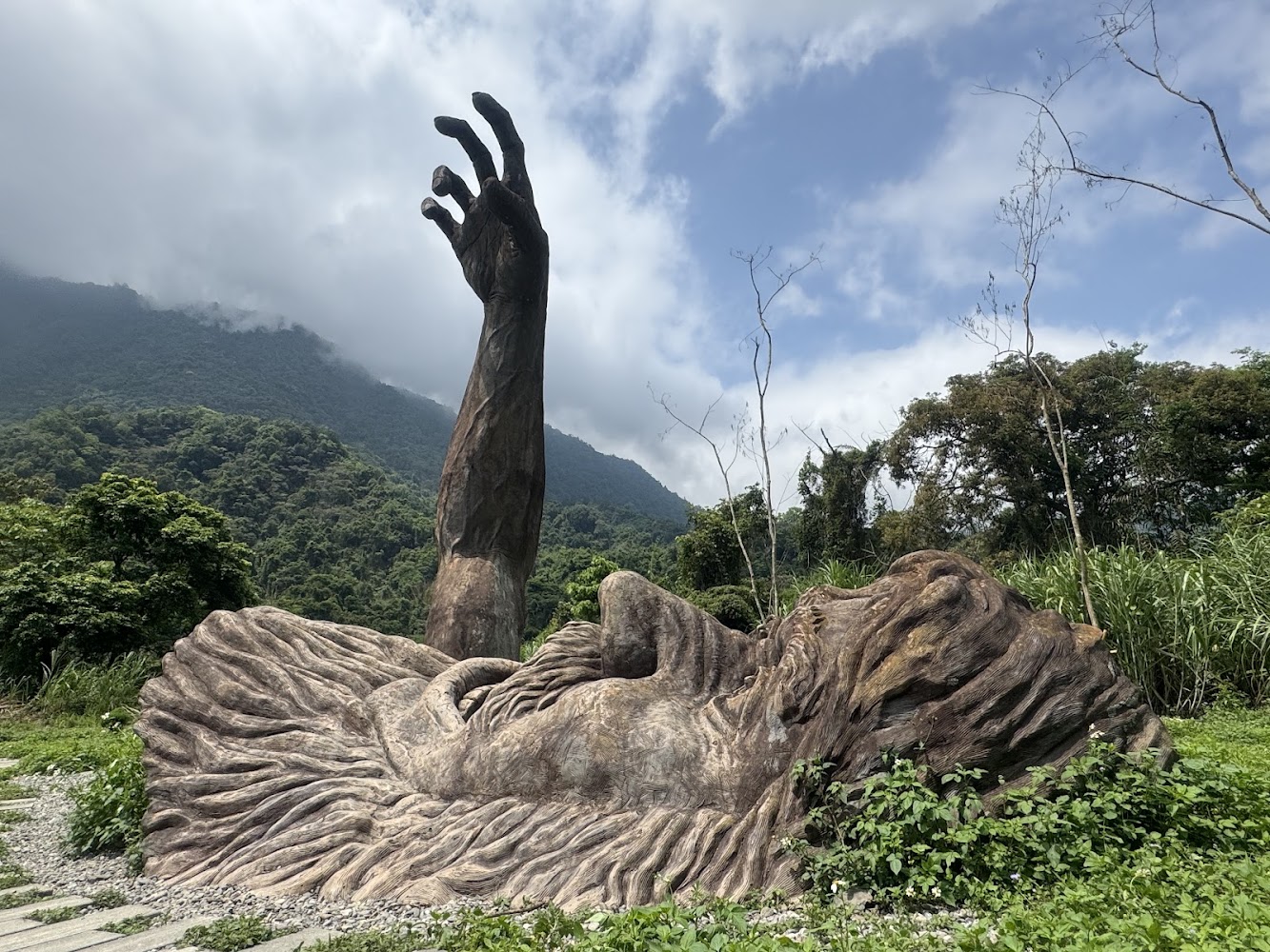 巨人之手雕塑仰躺於山林環境中