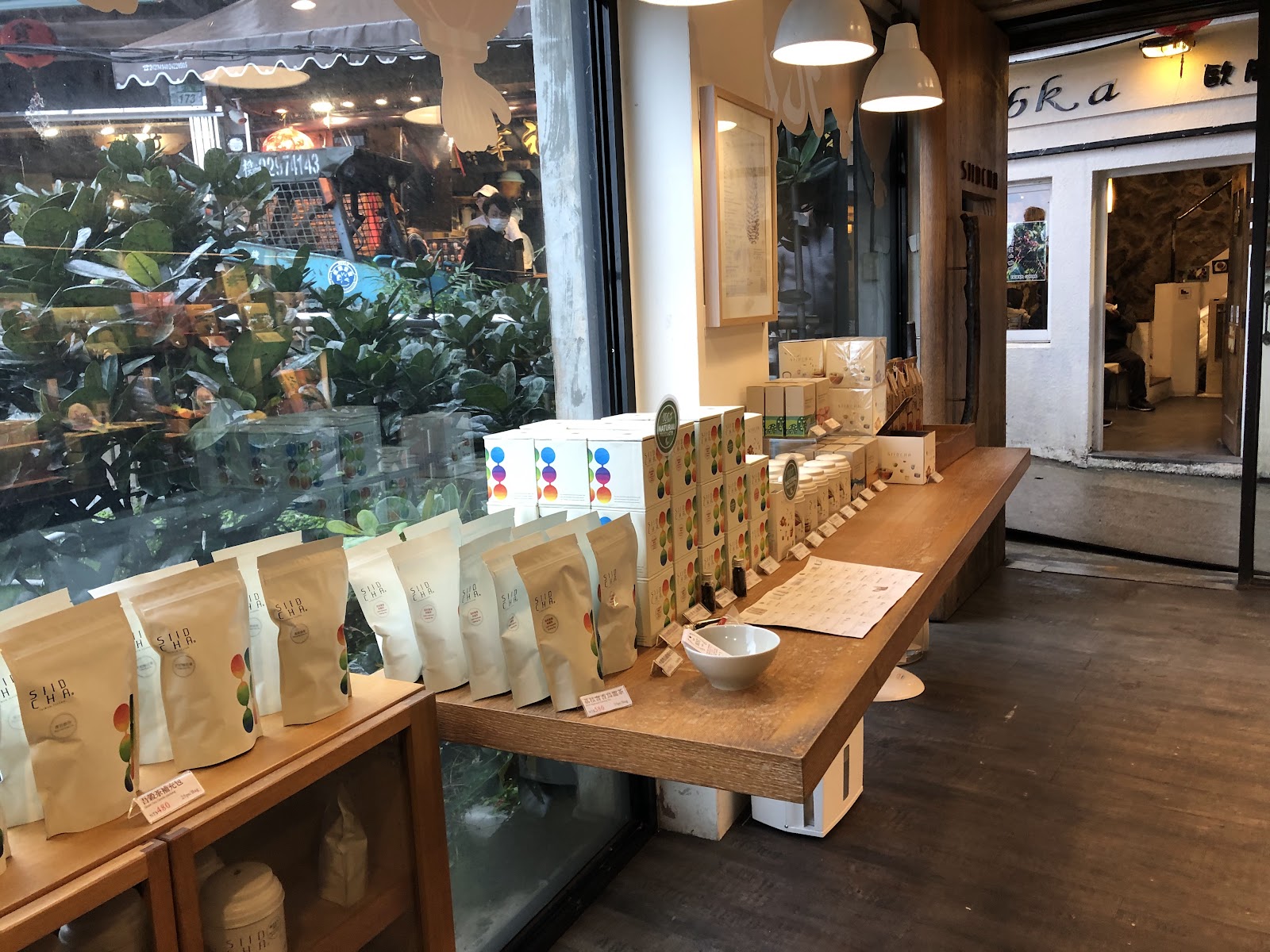九份茶葉專賣店內部，木桌陳列各式茶品包裝，落地窗外可見老街燈光