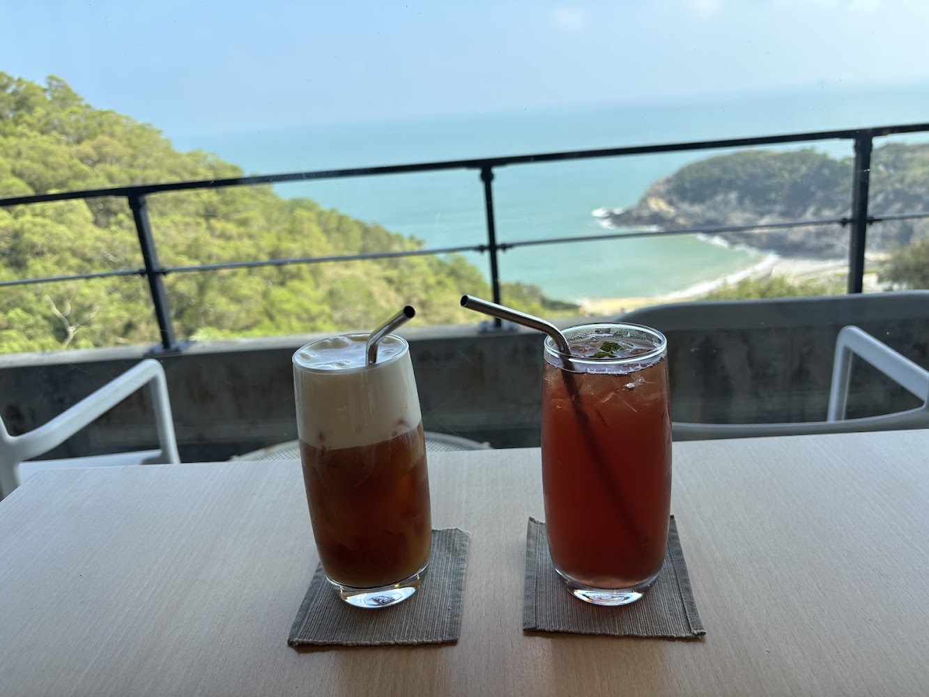 兩杯飲品放在桌上，背景是壯麗海景與綠色山丘