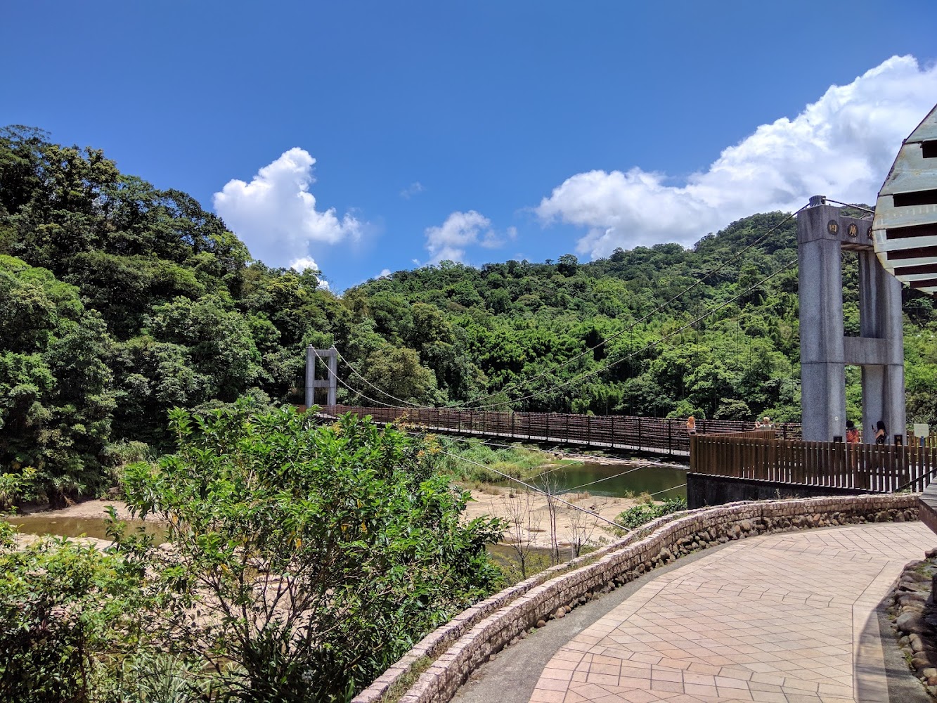 這張圖片主要有一座吊橋，橫跨在河流上，周圍是綠意盎然的山林和清澈的藍天，環境自然清新，是適合散步和欣賞風景的地方。