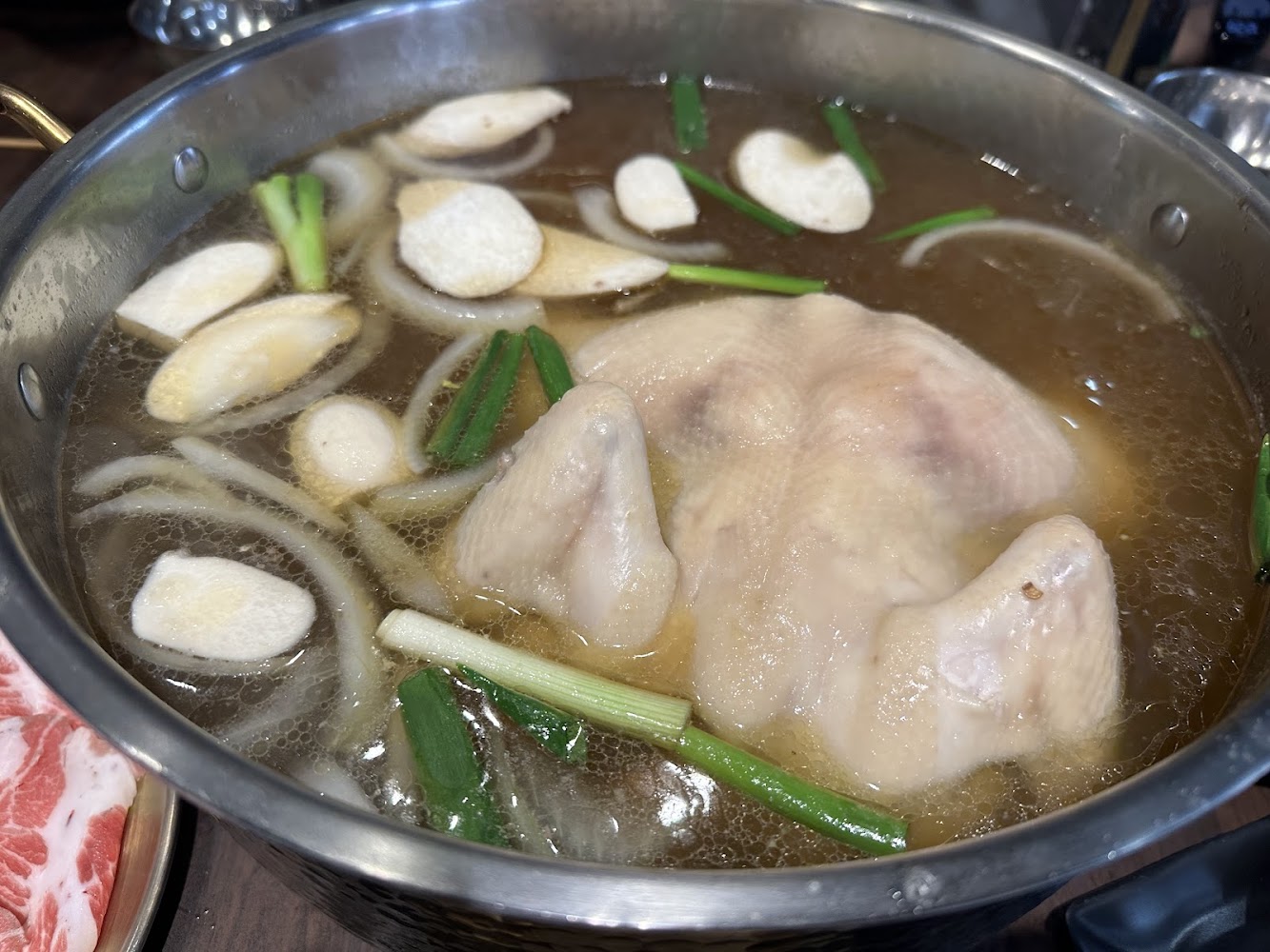 一鍋整隻雞湯，內有蔥段與蒜片，湯頭清澈