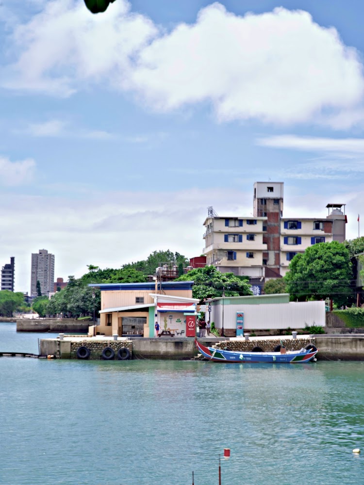 河岸邊停著彩色小船，旁邊有民宅與藍天白雲