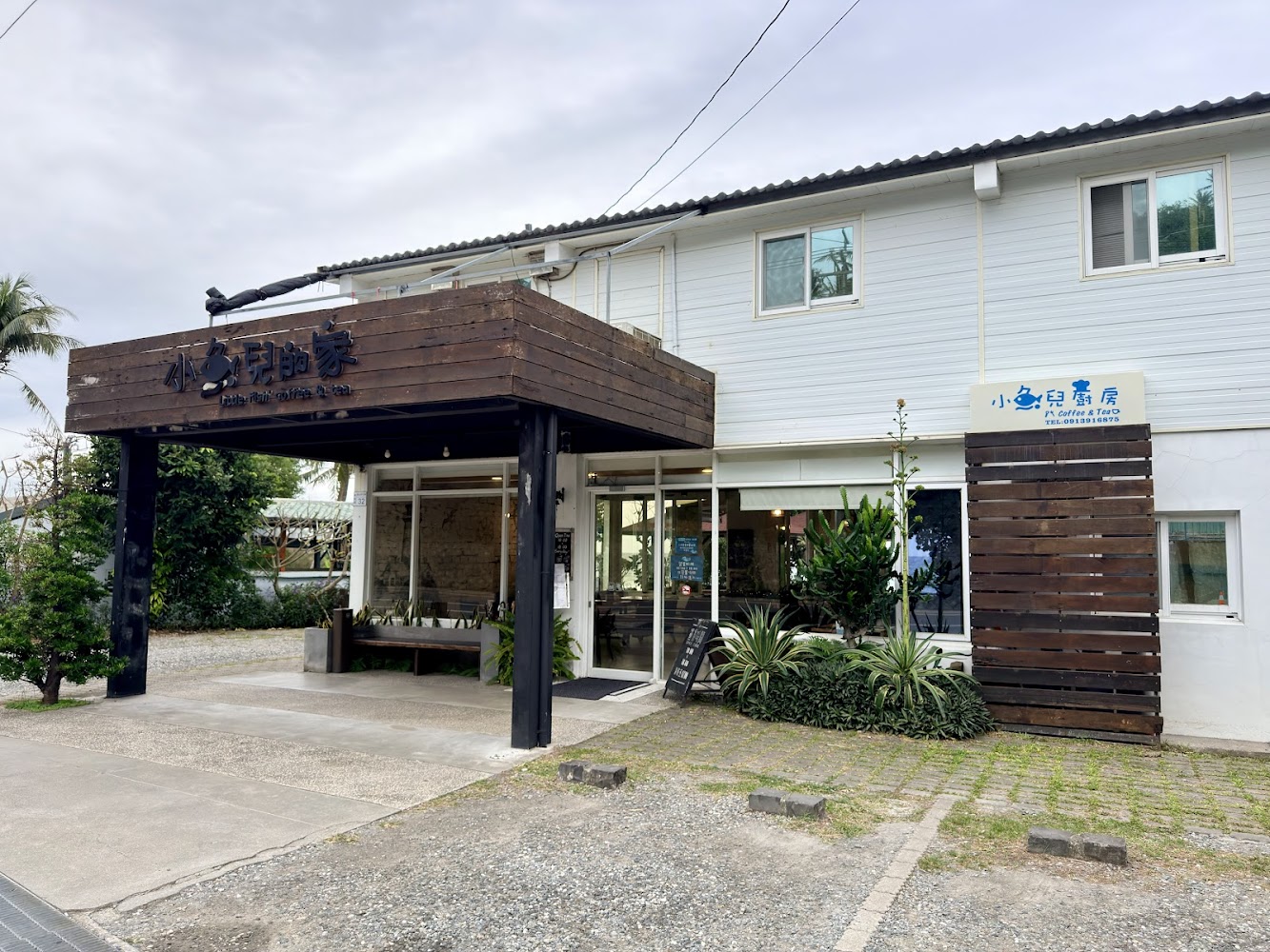 名為小魚兒的家咖啡館，外觀以白色牆面和木質裝飾為主，門口有綠色植栽點綴