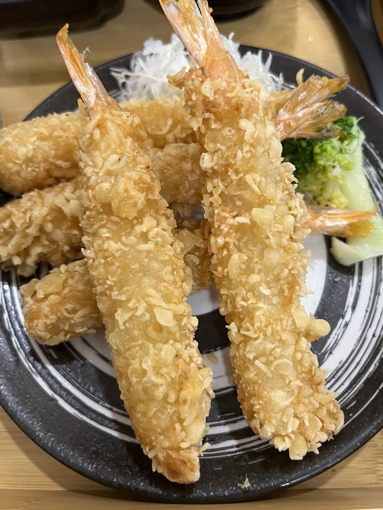 這張圖片主要展示了一盤金黃酥脆的炸蝦天婦羅，旁邊搭配了些許蔬菜和白蘿蔔絲，看起來色澤誘人、外皮酥脆，是一道常見的日式料理。