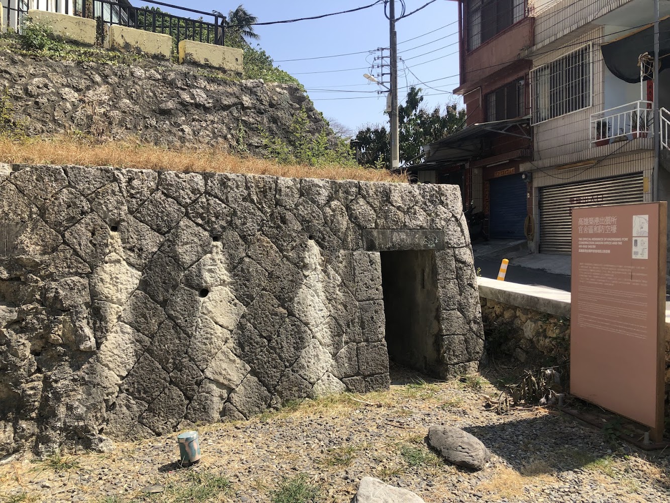 石塊建成的地下避難設施入口旁有說明牌，位於都市角落。