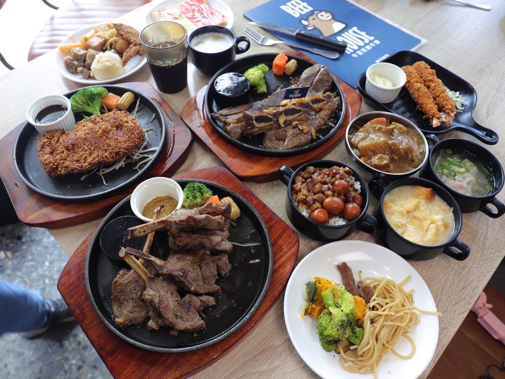 桌上擺滿牛排、羊排、炸豬排、蝦排、燉飯、湯品、小菜與飲料，適合多人聚餐。
