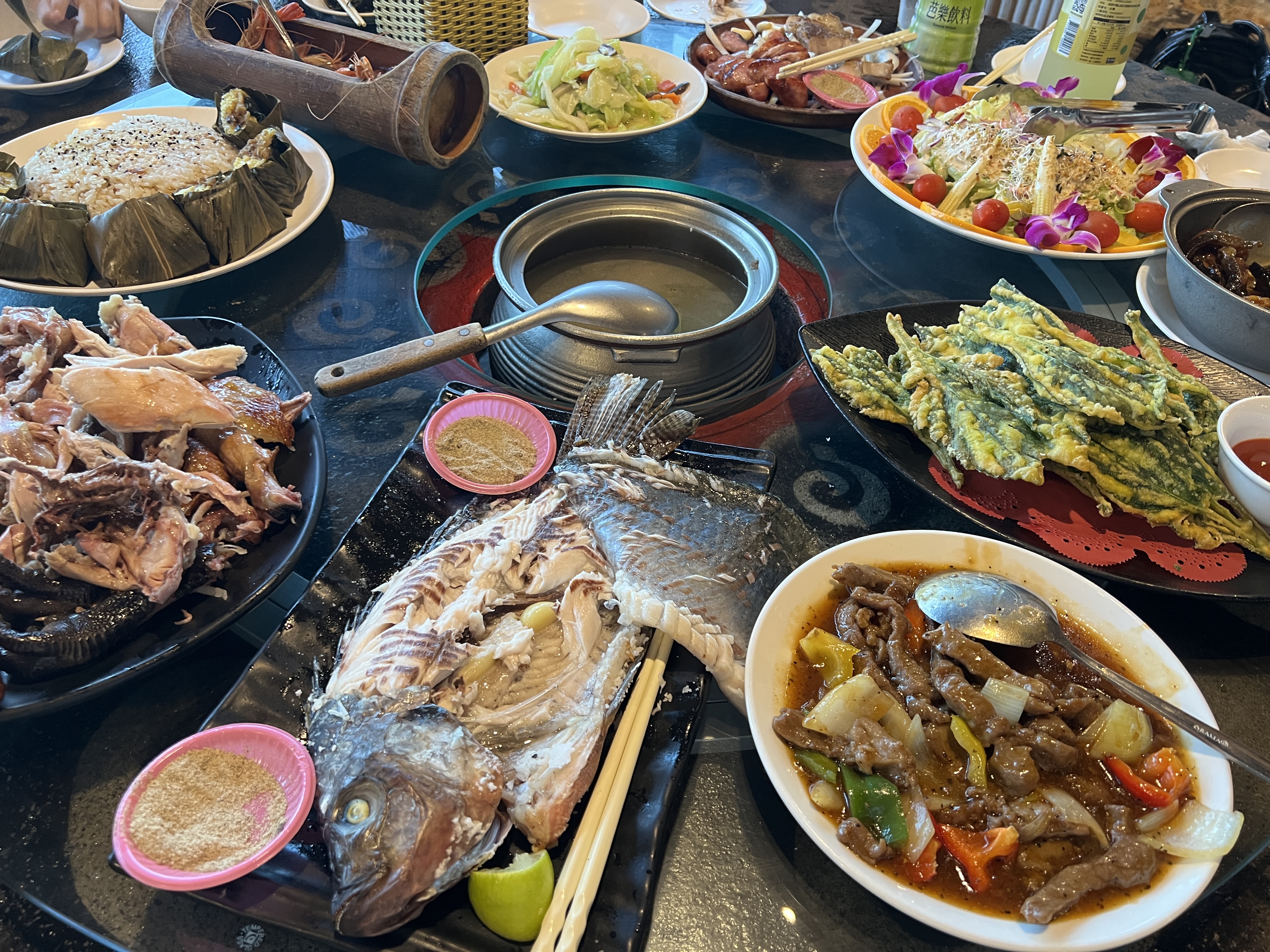 一桌豐富的中式桌菜，包括烤魚、炒肉、野菜煎餅、竹筒飯、蔬菜沙拉和烤雞等