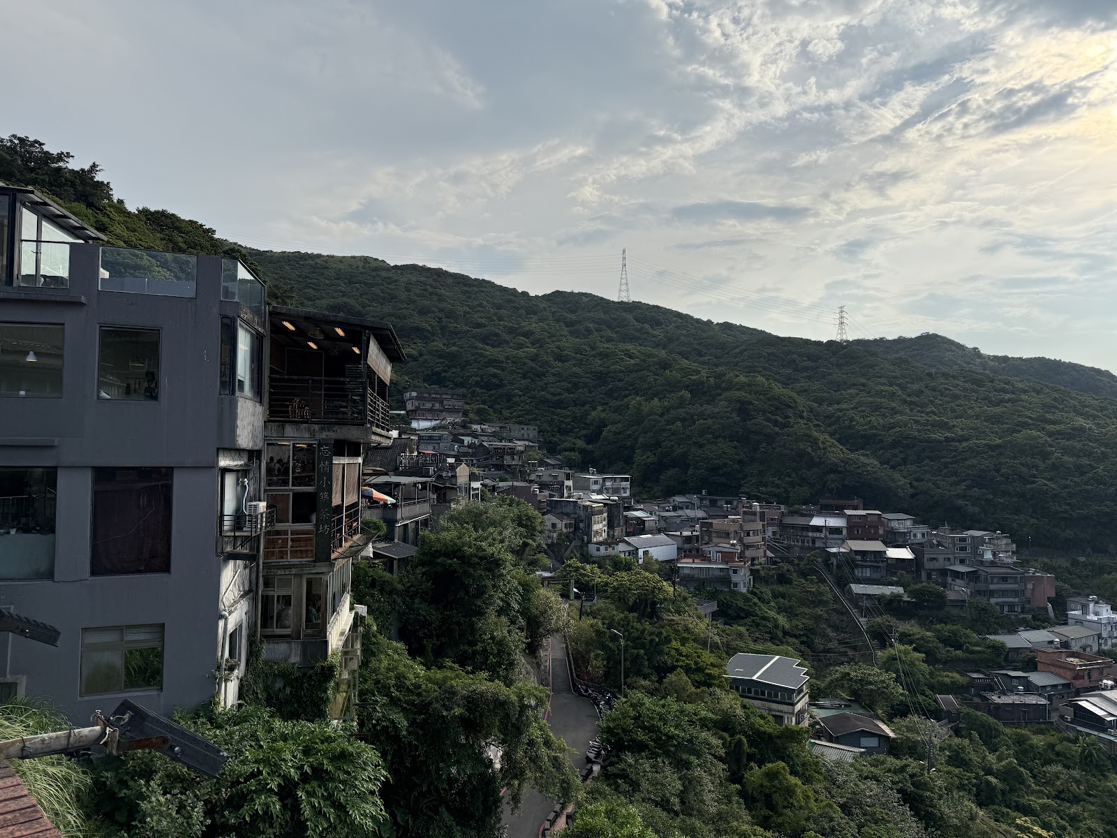九份山坡側面多層樓房沿山坡而建，傍晚柔光，背景翠綠山丘
