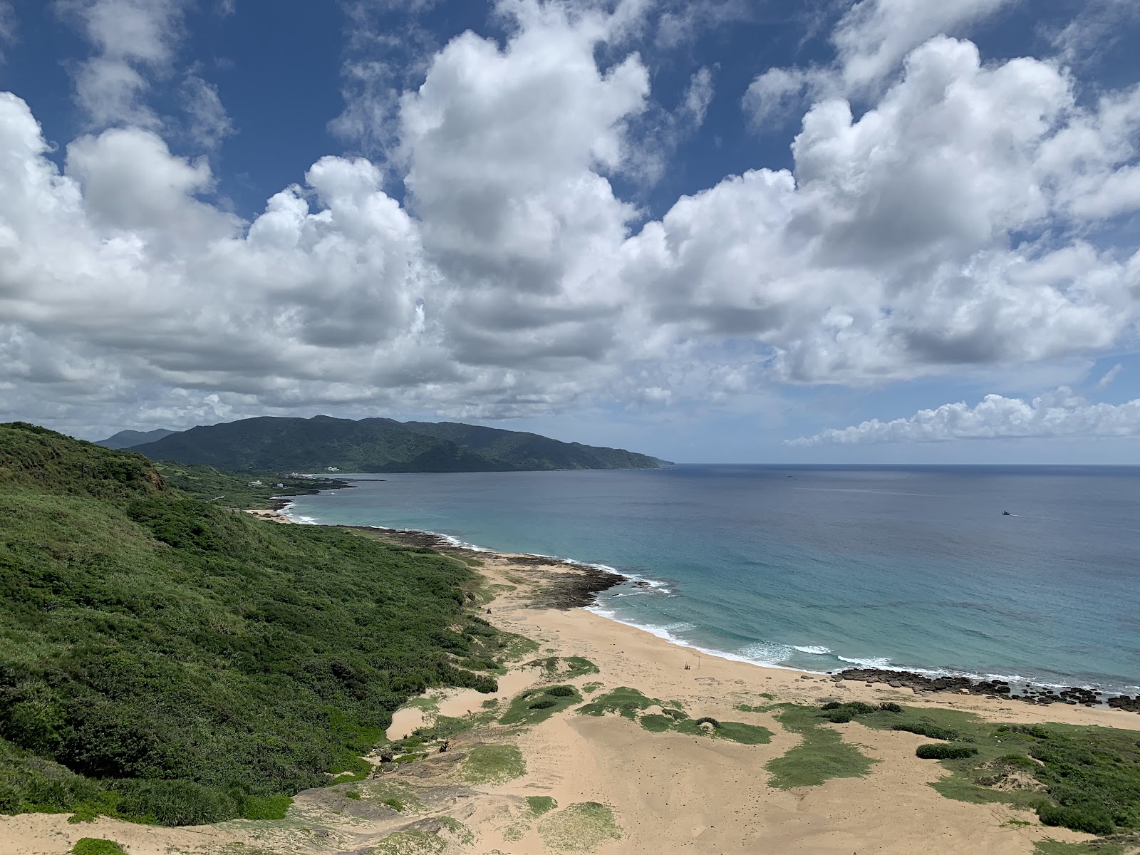 高處俯瞰風吹砂，金色沙洲、黑色礁岩與湛藍海洋的鮮明對比，翠綠山丘環繞