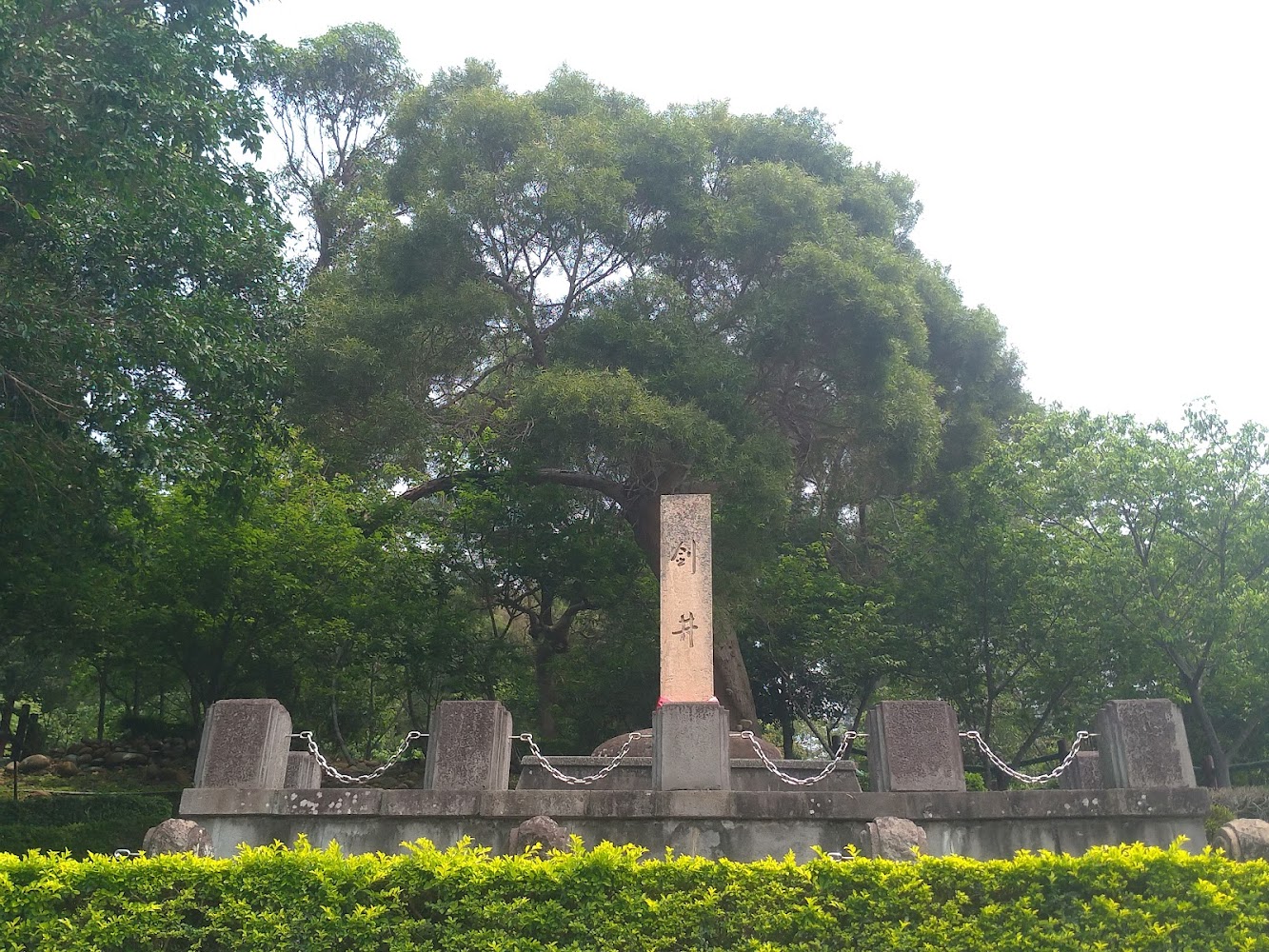 公園中的石碑周圍有石柱和鐵鍊背景為樹木