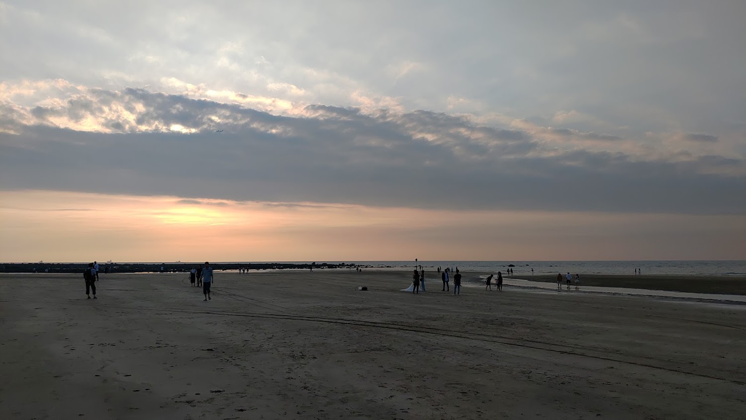 夕陽西下天空布滿雲彩，沙灘上三五成群遊客散步欣賞海景