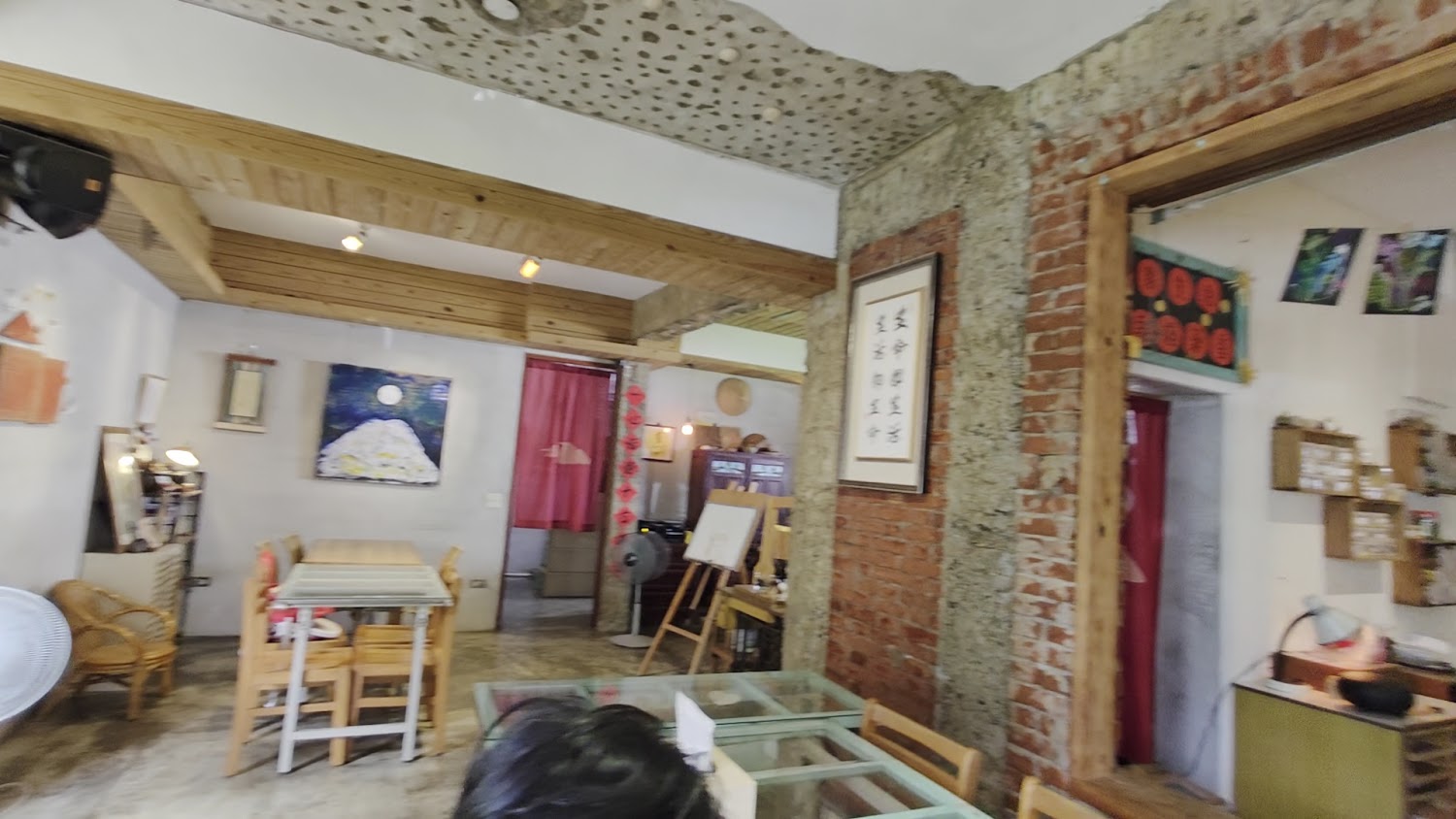 這是一間帶有紅磚與水泥元素的咖啡廳或小店，室內擺放木質桌椅及藝術裝飾，氣氛溫馨文藝。