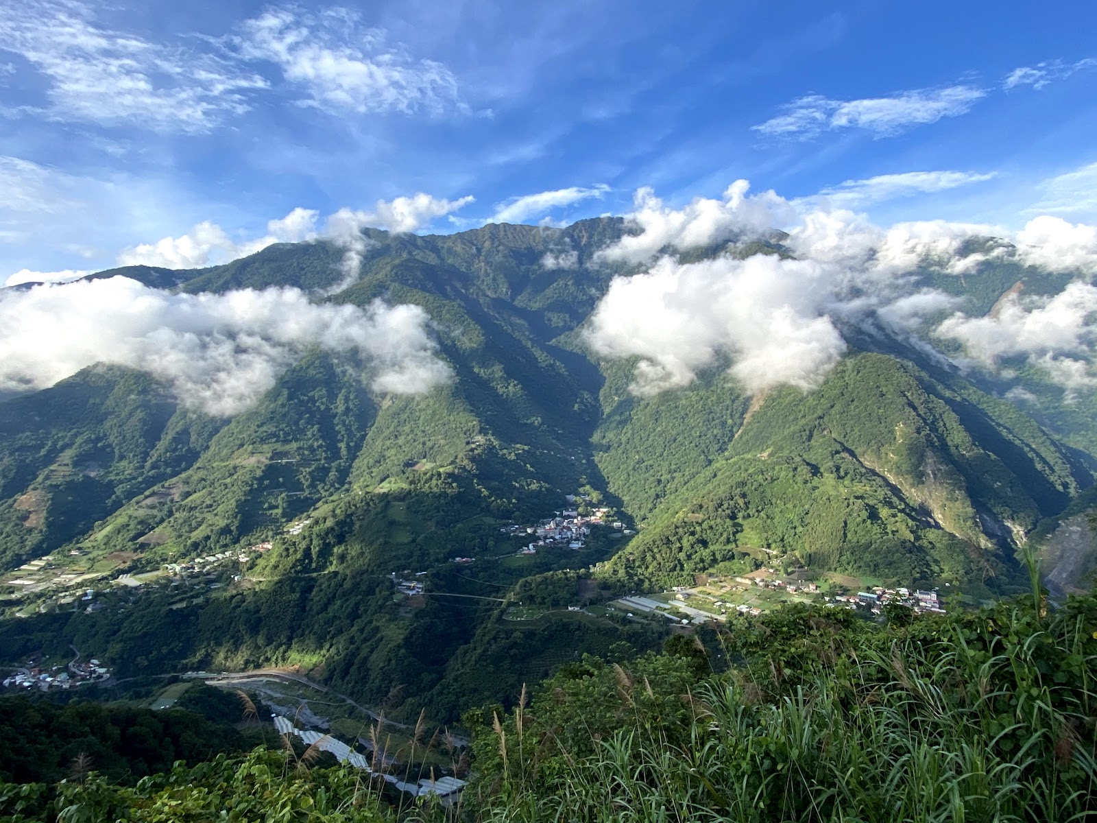 信義鄉山區全景，雲朵纏繞山腰，山腰散布部落建築，溪谷蜿蜒其間