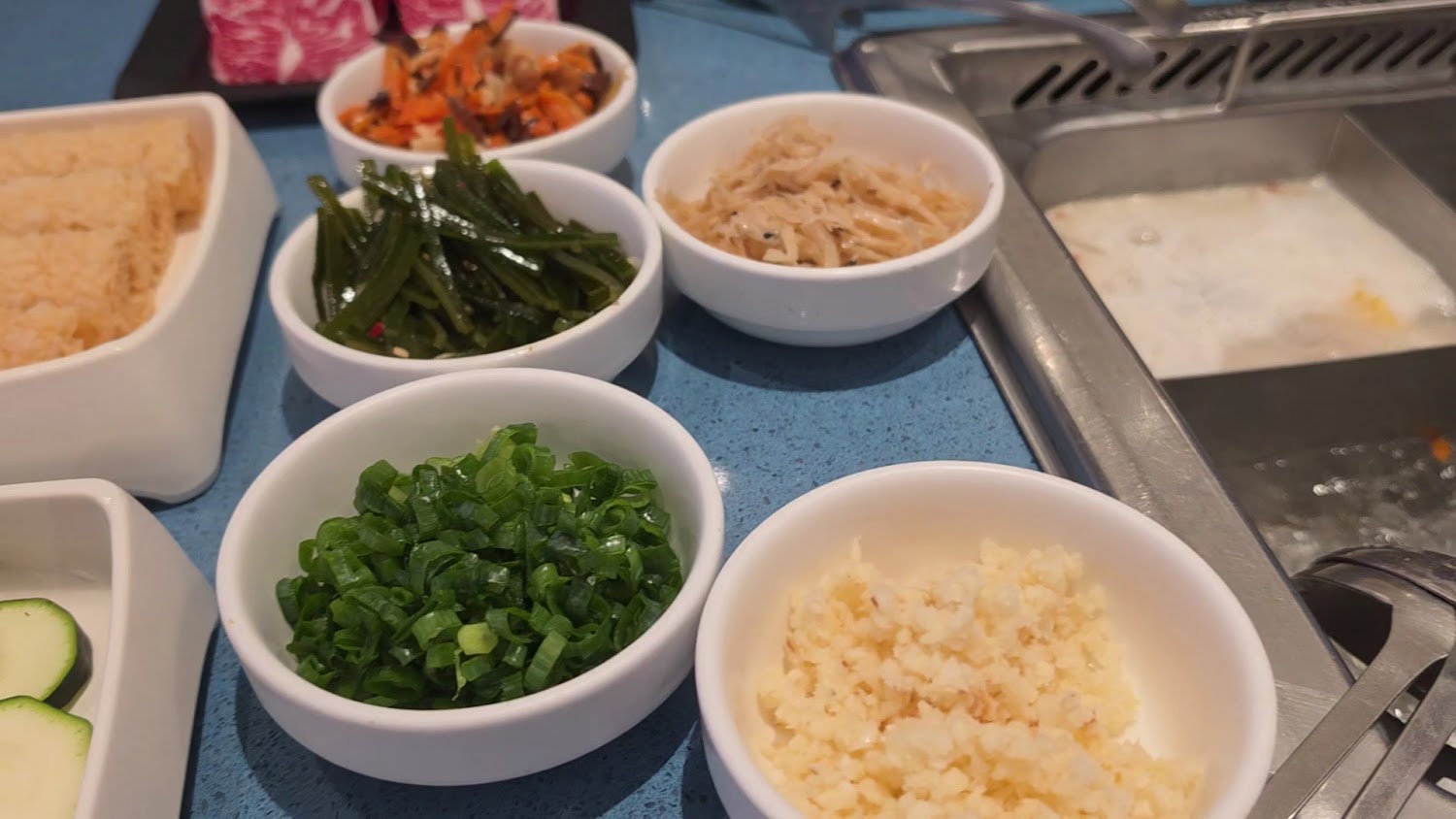 多種火鍋配料與醬料小菜，旁邊可見鍋底