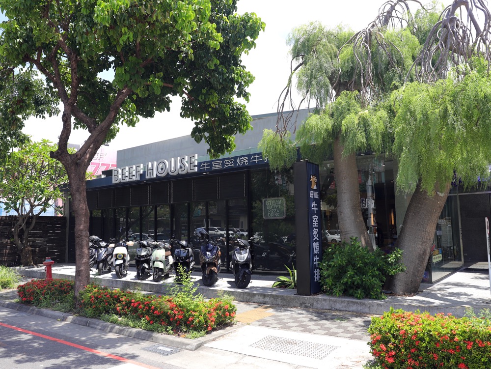 牛室炙燒牛排台南海安店外觀，門口前停放多台機車，周邊綠樹植栽環境清新。