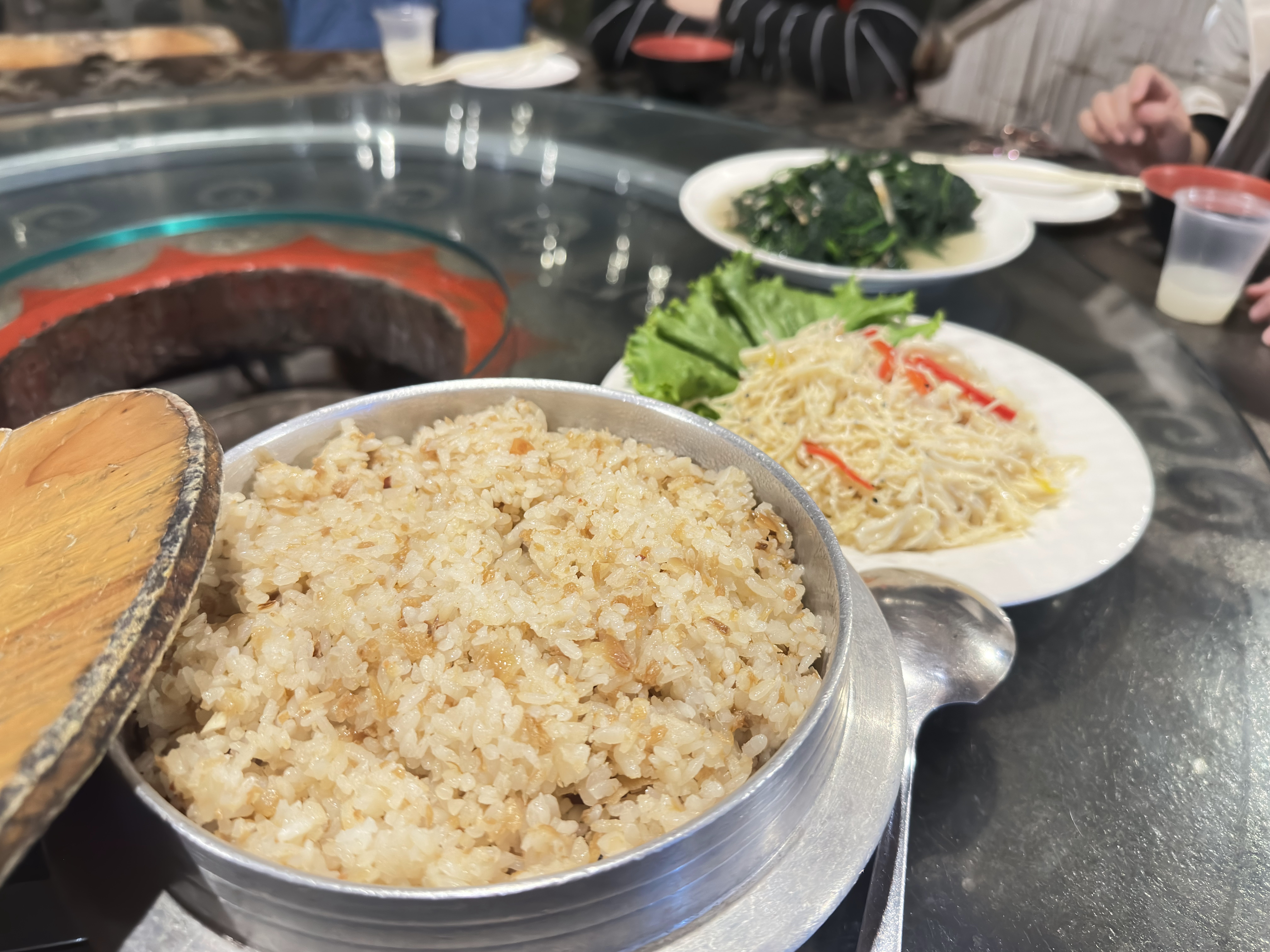 熱氣騰騰的米飯，旁邊有金針菇拌蔬菜和炒青菜，餐桌氛圍熱鬧