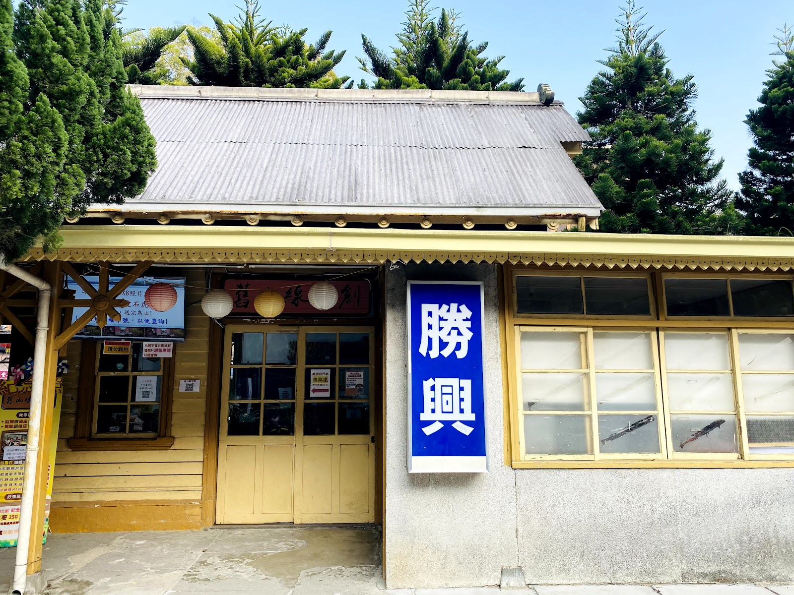 勝興車站正面，黃色木造站房，勝興藍色站牌，背景松樹藍天