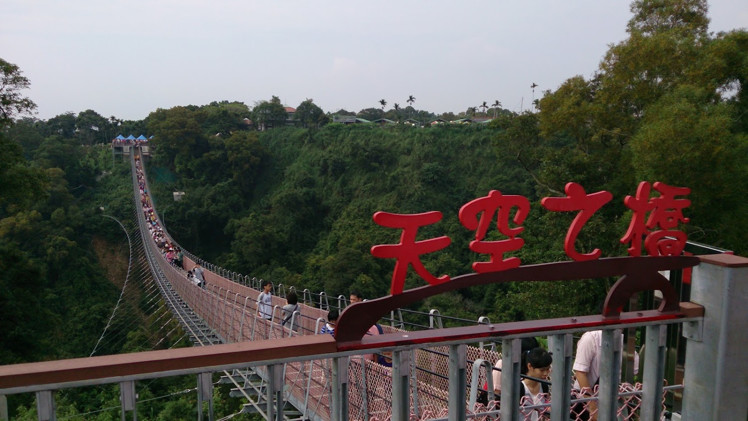 一座名為天空之橋的大型吊橋，橫跨於翠綠山谷上，許多遊客正步行於吊橋上，體驗壯麗自然景觀與高空行走的刺激。