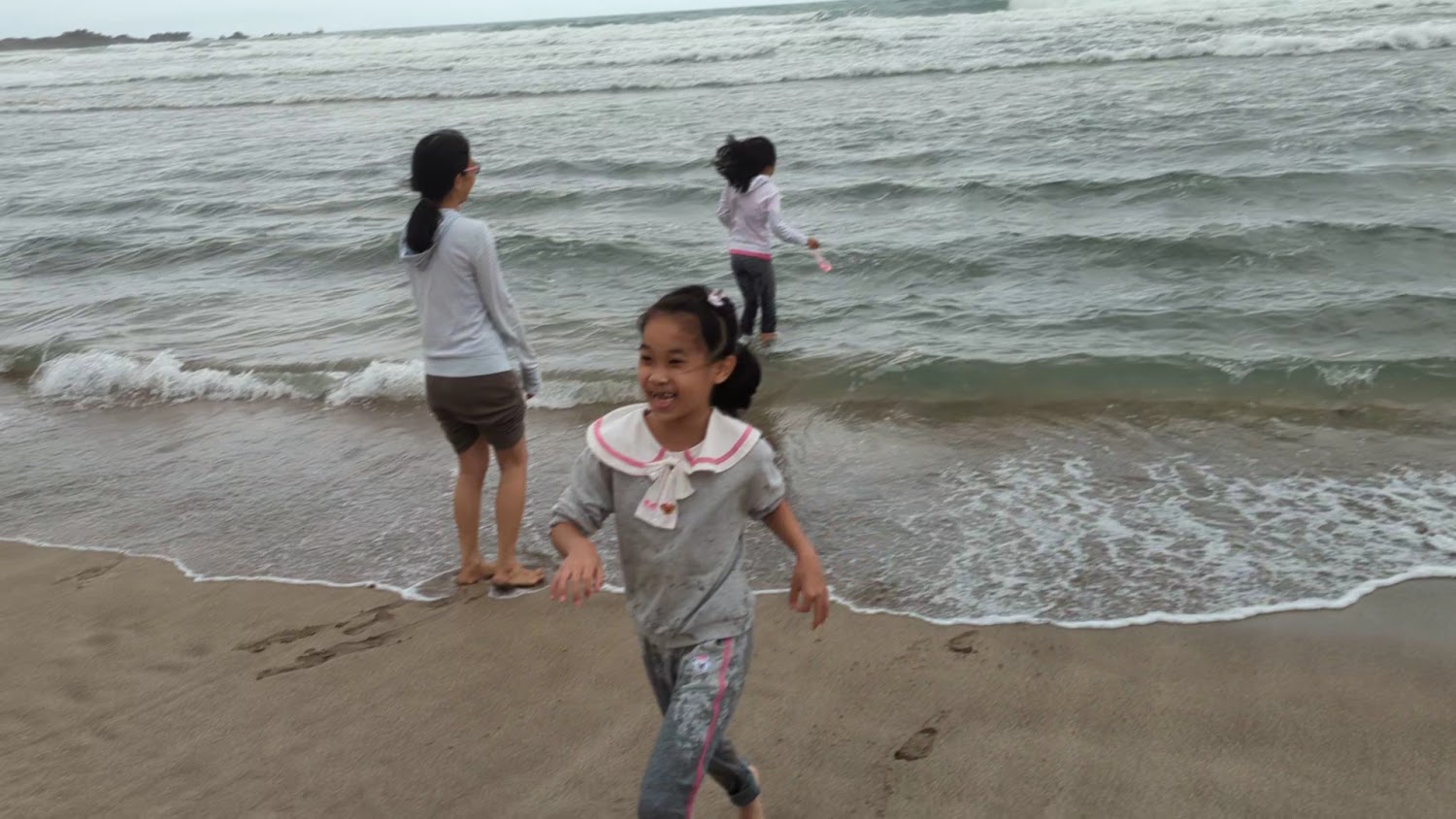 三位遊客在海邊踏浪，背景是翻滾海浪與藍海