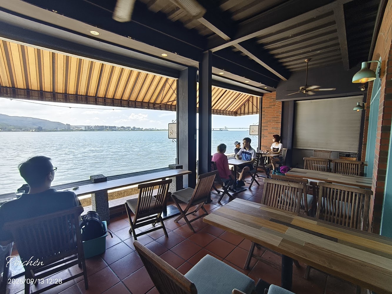 面海咖啡廳內有幾組客人坐在木製桌椅上，享受窗外海景和陽光