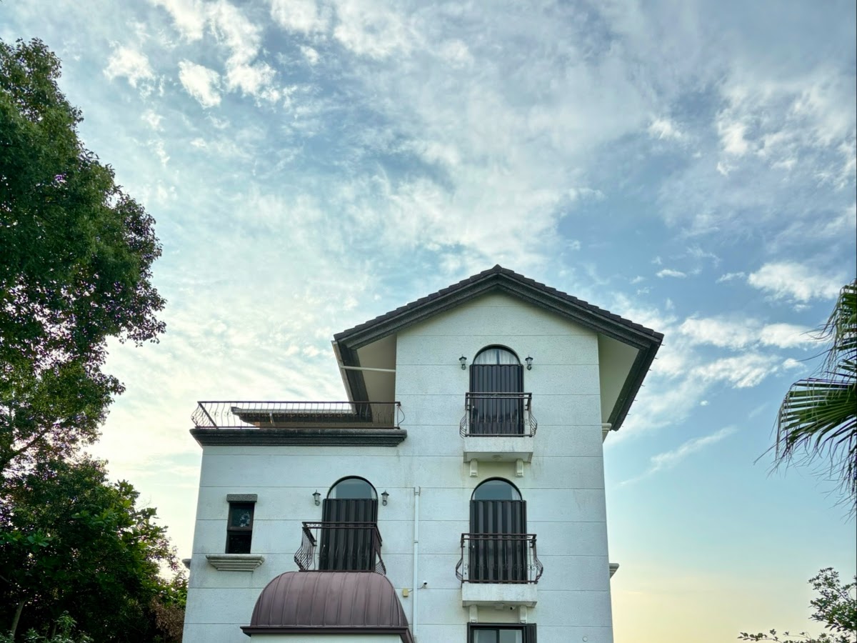 蘭天民宿白天三層歐式建築，拱形窗戶與鐵藝陽台，車庫旁停有白色轎車，藍天白雲