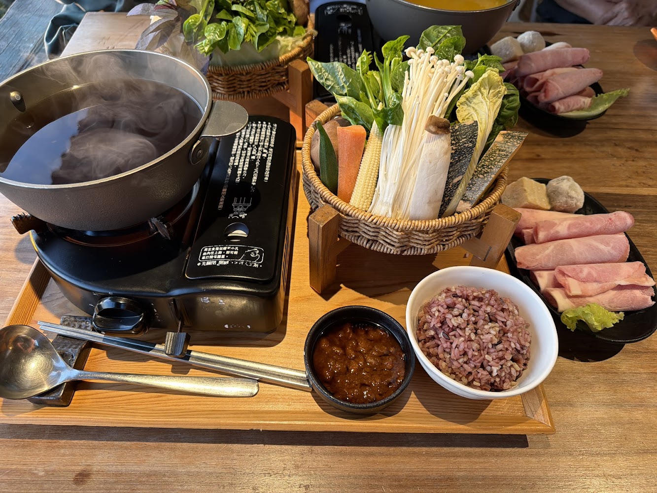 火鍋套餐，包括湯底、蔬菜拼盤、五穀飯、醬料與肉片
