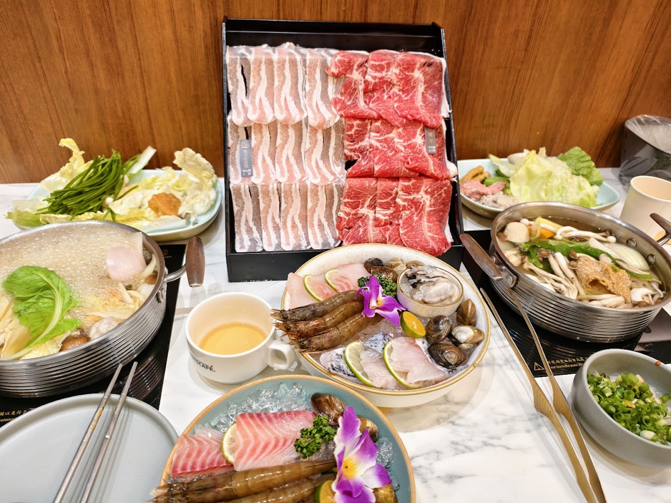 一桌豐盛火鍋料理，有肉片、海鮮、蔬菜及兩鍋湯底。