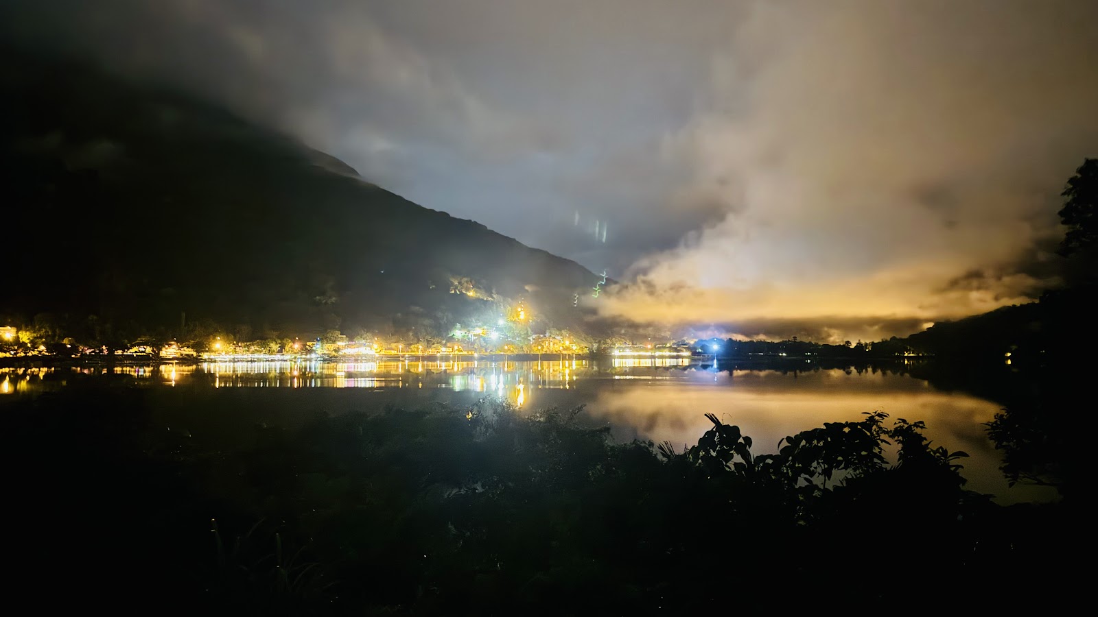 鯉魚潭夜景，湖畔金黃燈光倒映水面，雲間橙色霞光，霧氣飄散山間如夢似幻