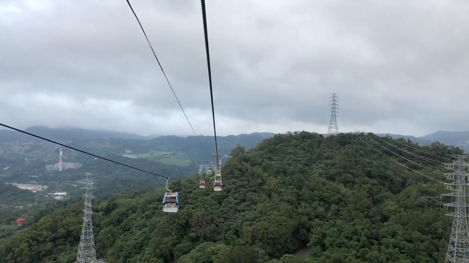 貓空纜車車廂內往外望，可見多台纜車廂懸掛山谷間，綠色山景連綿