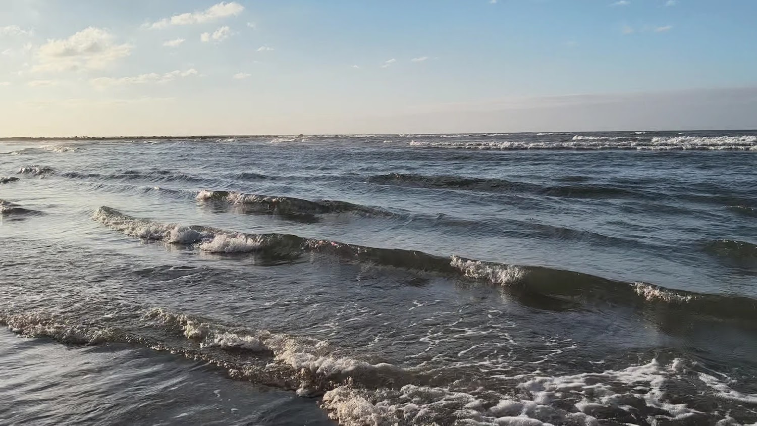 海浪輕拍岸邊、晴朗天空與白雲的沙崙海水浴場海邊景色