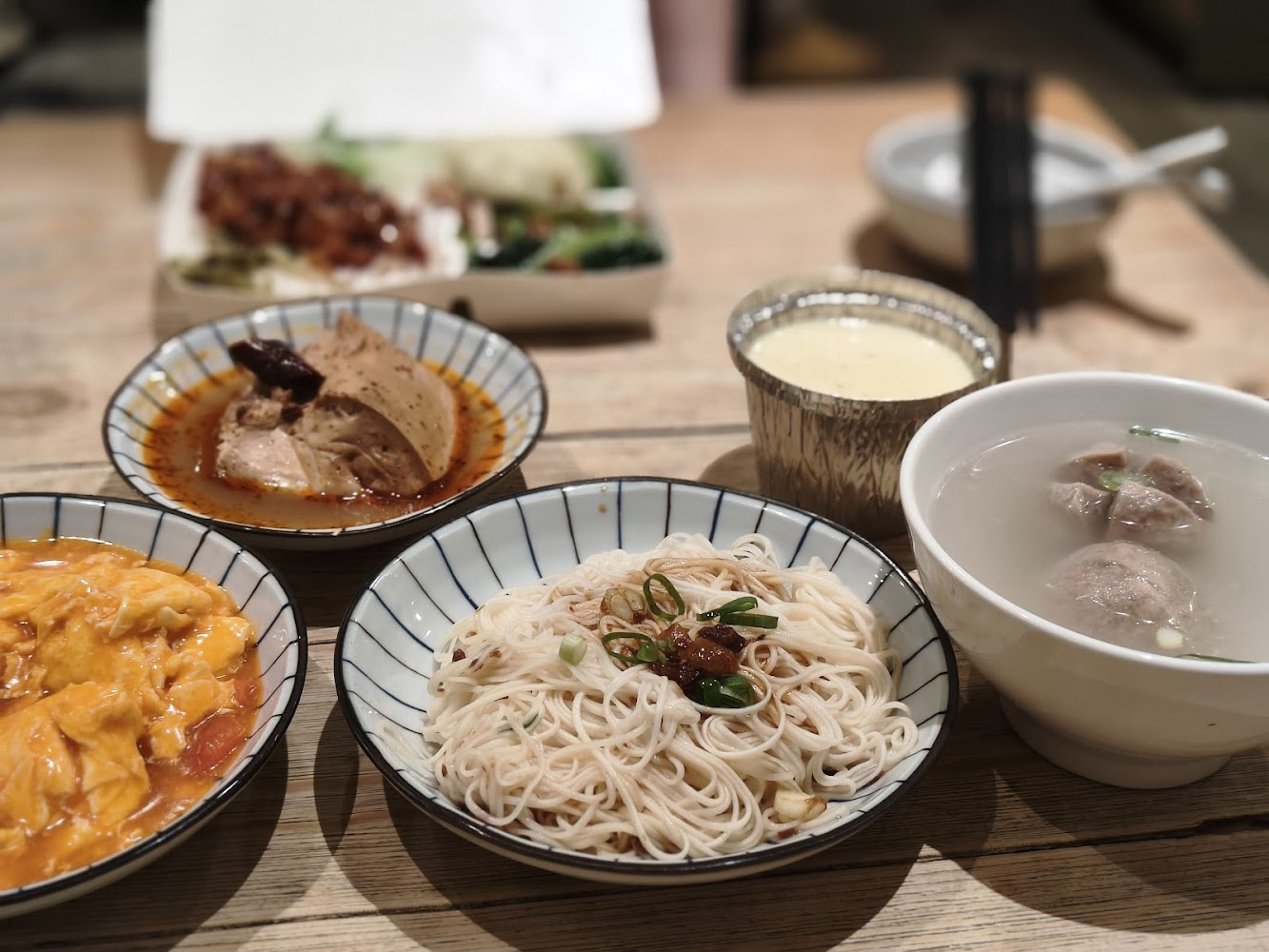 中式料理組合，有拌麵、番茄炒蛋、辣味雞腿、貢丸湯、蒸蛋與便當盒。