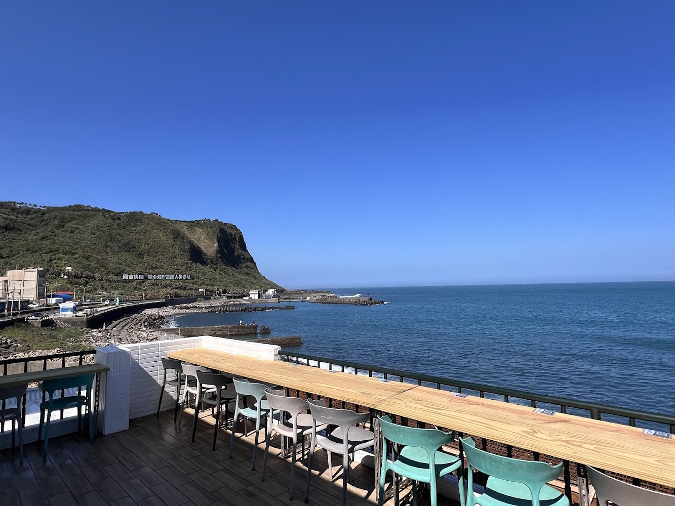 臨海戶外座位區有長型木桌與多張椅子，前方是廣闊海景