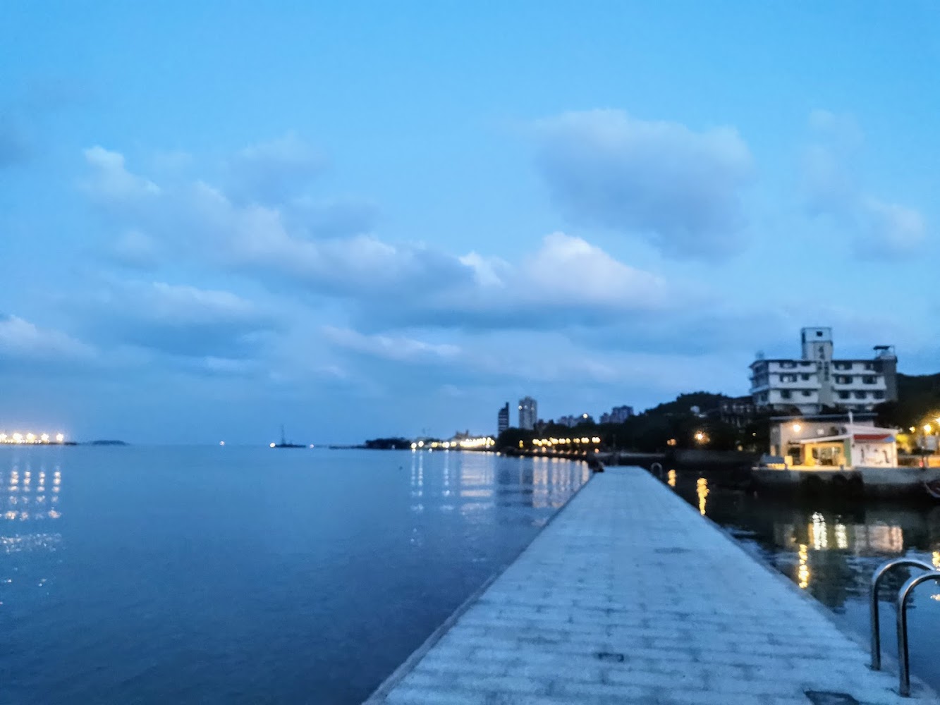 海邊碼頭與晚霞天空，遠處城市建築及岸邊燈光民宅