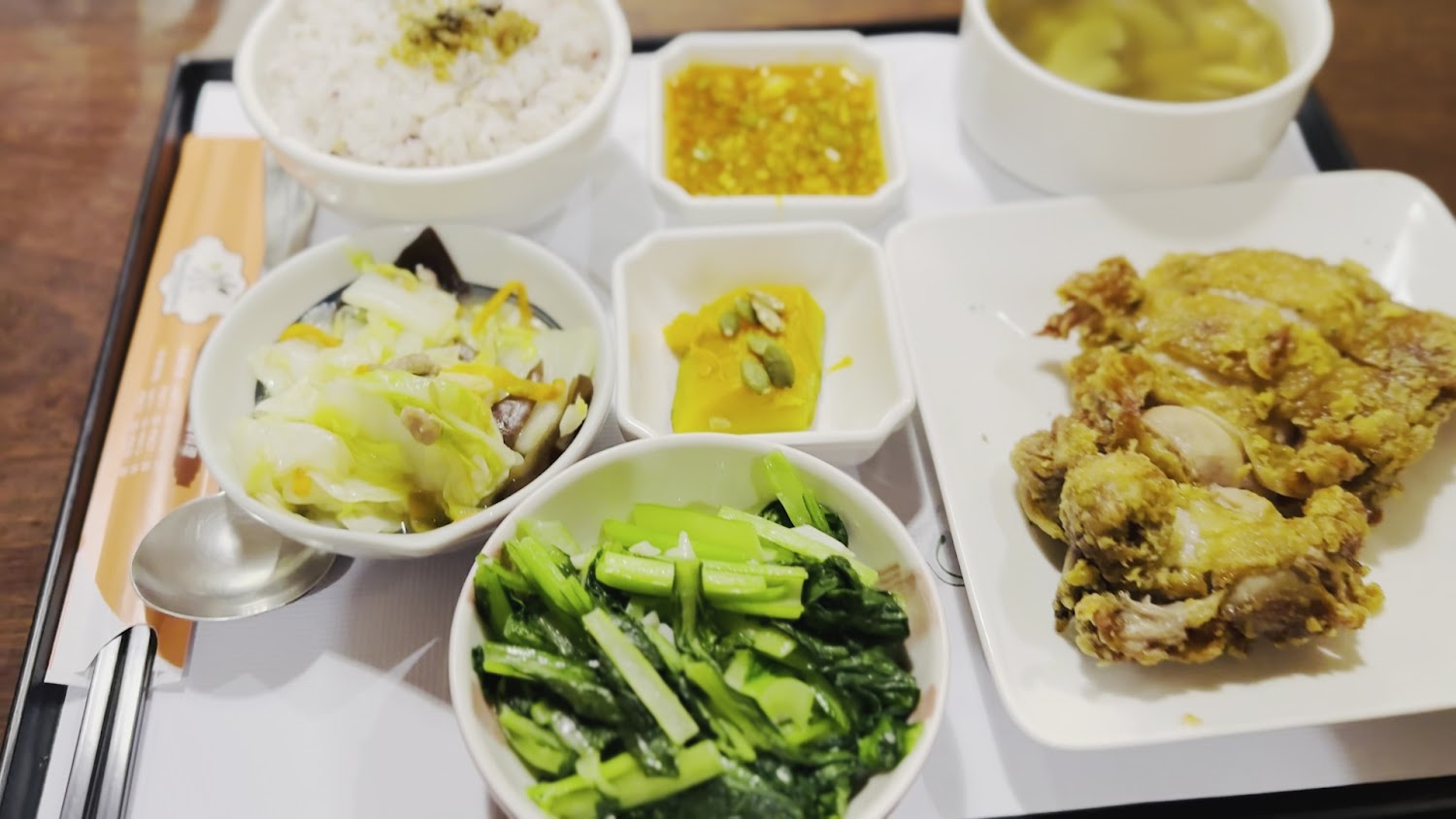 這張圖片是一份中式便當，包括炸雞腿、白飯、兩種青菜、小南瓜、湯品及沾醬，色彩豐富、營養均衡。