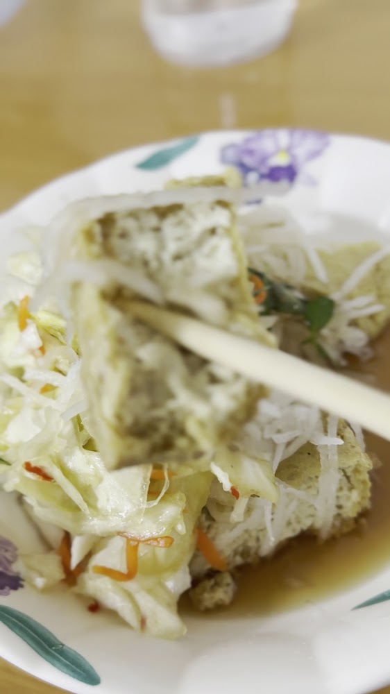 筷子夾起鋪有泡菜與醬汁的臭豆腐