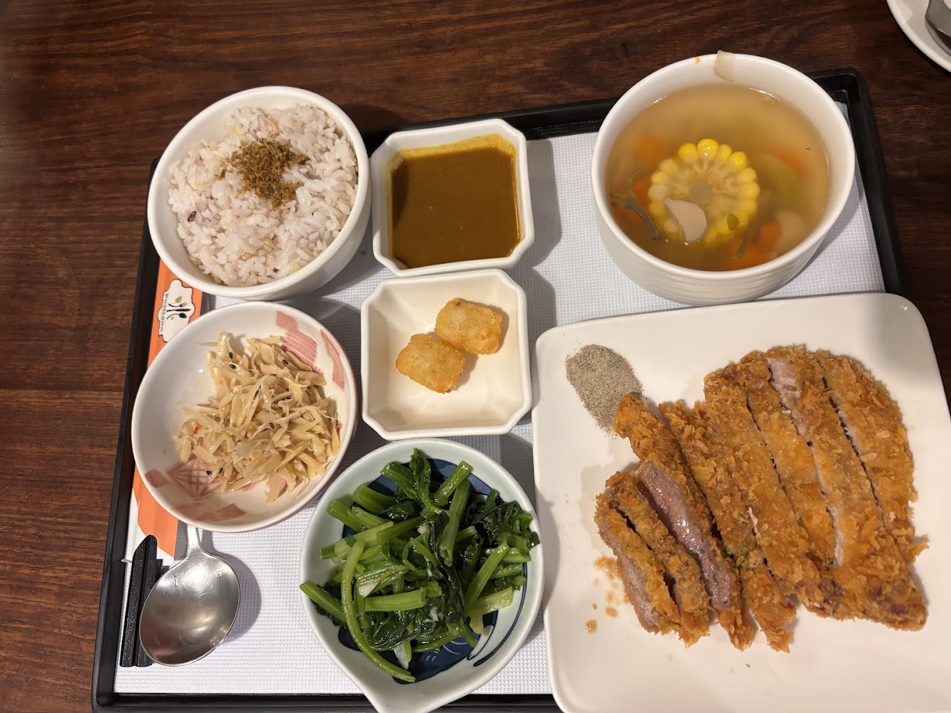 這張圖片主要是一份日式豬排定食，包括酥脆豬排、白飯、味增湯、醬料、炸薯餅、小菜、青菜及涼拌竹筍，是一套豐富且均衡的餐點。