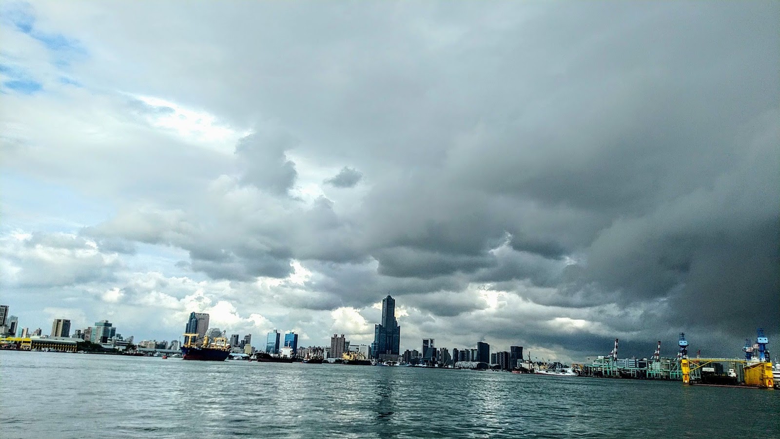 從旗津渡輪視角看高雄市區天際線，85大樓高聳入雲，烏雲層疊