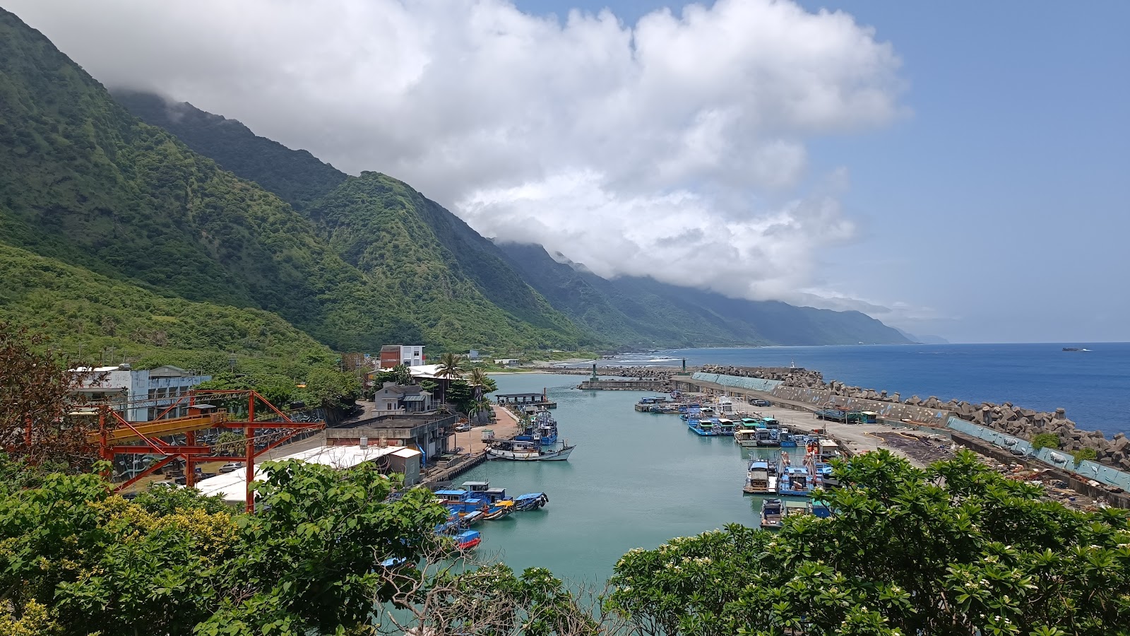 石梯漁港晴天全景，翠綠山壁、停泊漁船、翡翠海灣與藍天白雲